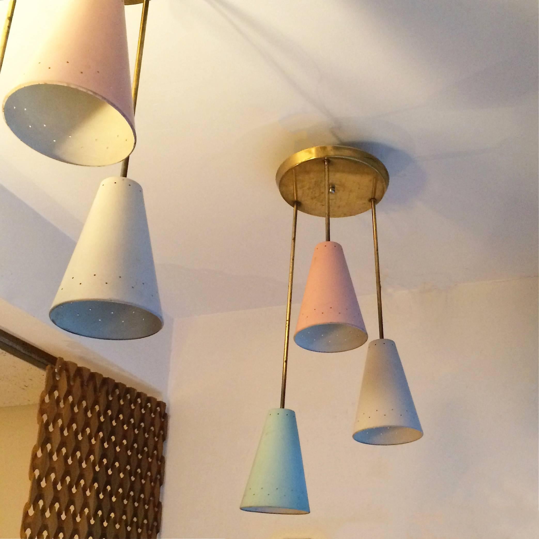 Mid-Century Modern pendant lights featuring a graduated cluster of three pastel pink, blue and white, perforated cones on brass poles mounted on circular plates. Four clusters are available.