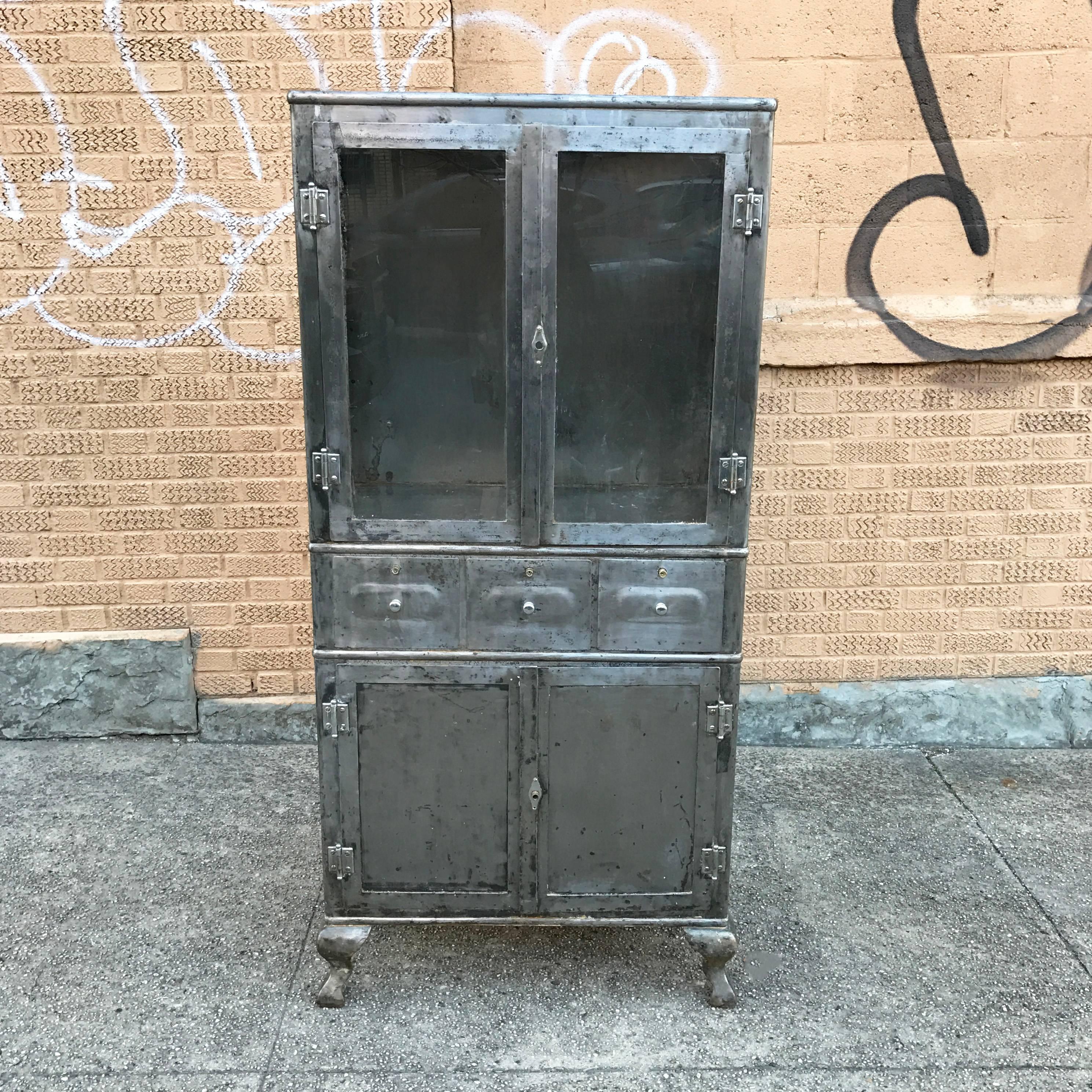 1920s, Industrial, brushed steel, double door, apothecary, medicine cabinet has cabinet and drawer storage below and display on top with two glass shelves.

