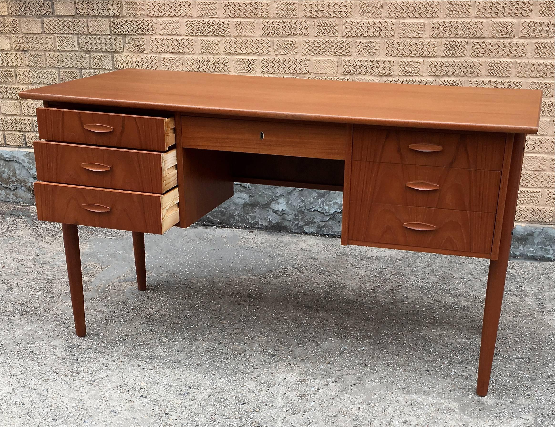 Danish modern, teak desk has storage on either side and a drawer in the middle. The desk features a finished front with an open shelf for display or books. The sitting clearance is 17 inches w x 25 inches ht.

                              