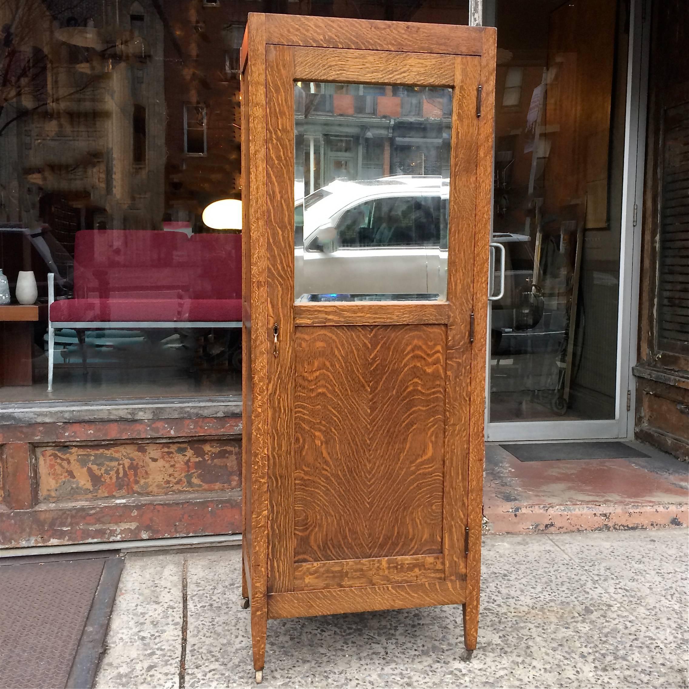 1920s, Art and crafts armoire is quarter sawn oak with a beveled mirror front panel. The open interior space measures 24.5 inches W x 18.5 inches D x 64.5 inches height with a retractable rail for hanging clothes.