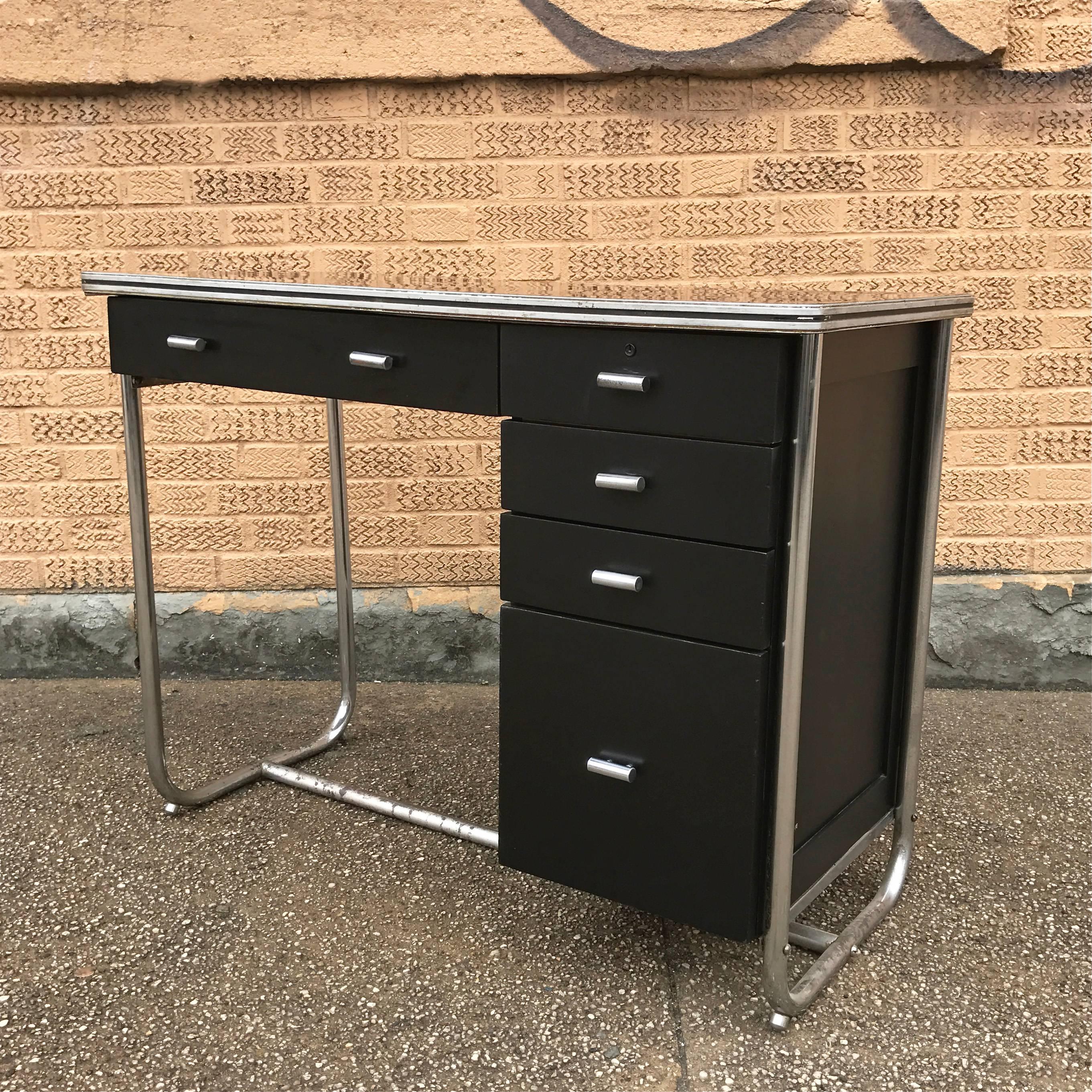 Art Deco, machine age, tubular chrome, lacquered wood and laminate desk designed by Gilbert Rohde for Troy Sunshade features five drawers and an architectural glass front cabinet with display shelves on reverse side making the desk presentable on