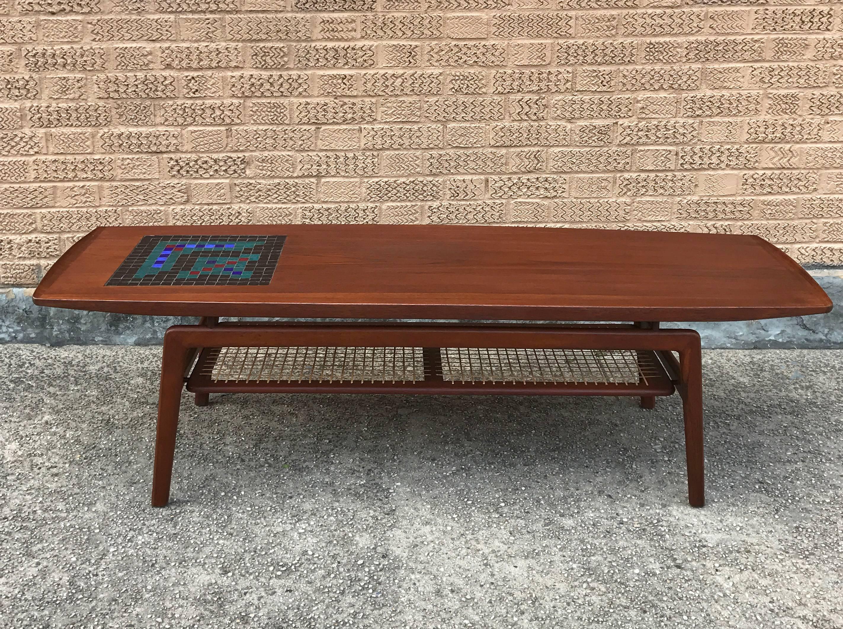 Danish modern, teak coffee table featuring a ceramic mosaic inlay detail and caned magazine shelf designed by Arne Hovmand-Olsen for Mogens Koch. The magazine rack has 9