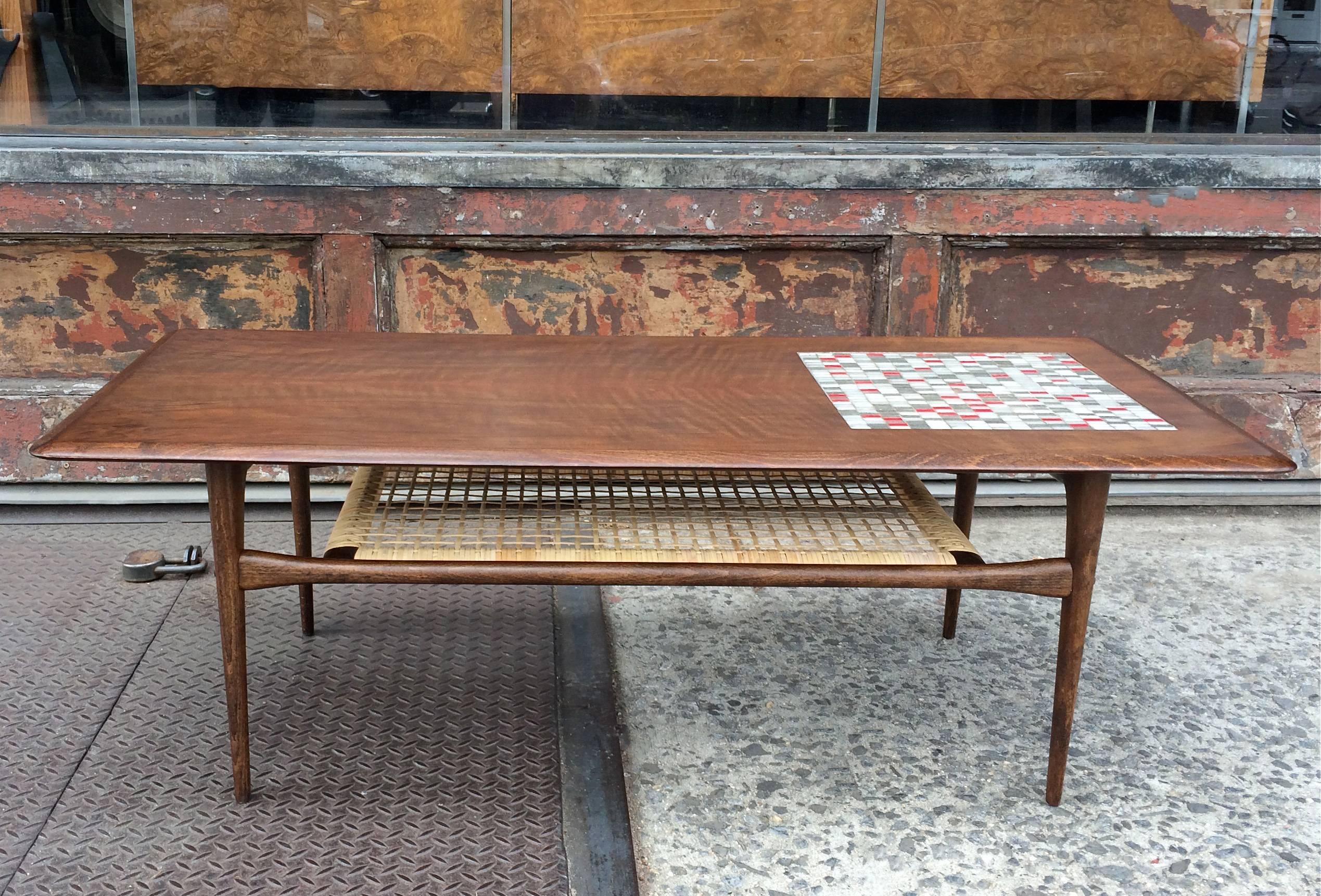 Danish modern, beveled edge, walnut coffee table features a ceramic tile mosaic inlay and caned magazine shelf below attributed to Arne Hovmand Olsen.