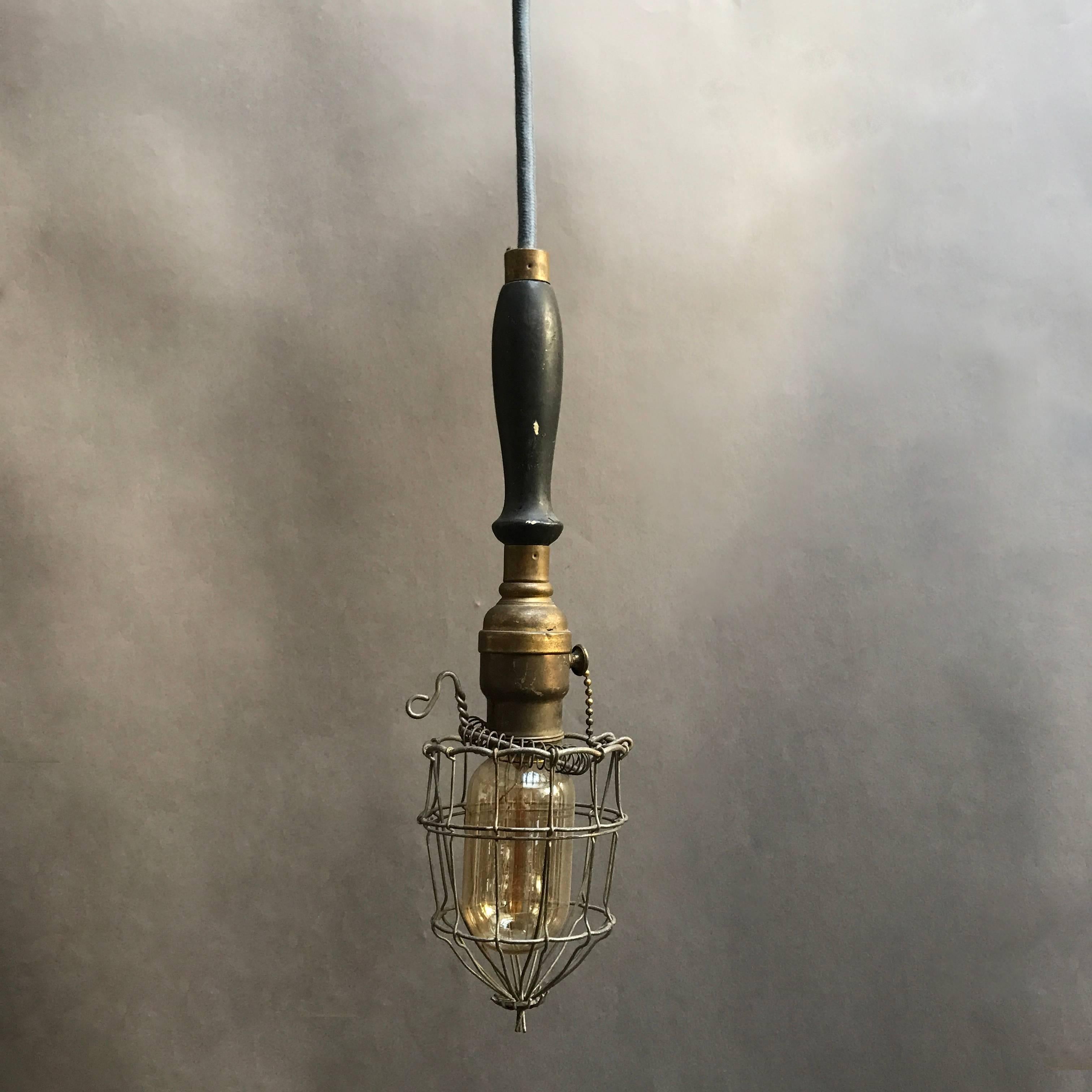 Early 20th century, Industrial, caged, utility light features a brass fitter and hardware with pull chain and black, lacquered maple handle. This light is wired for 200 watts and has 68? of wire with plug and can also be used as a wall sconce hung
