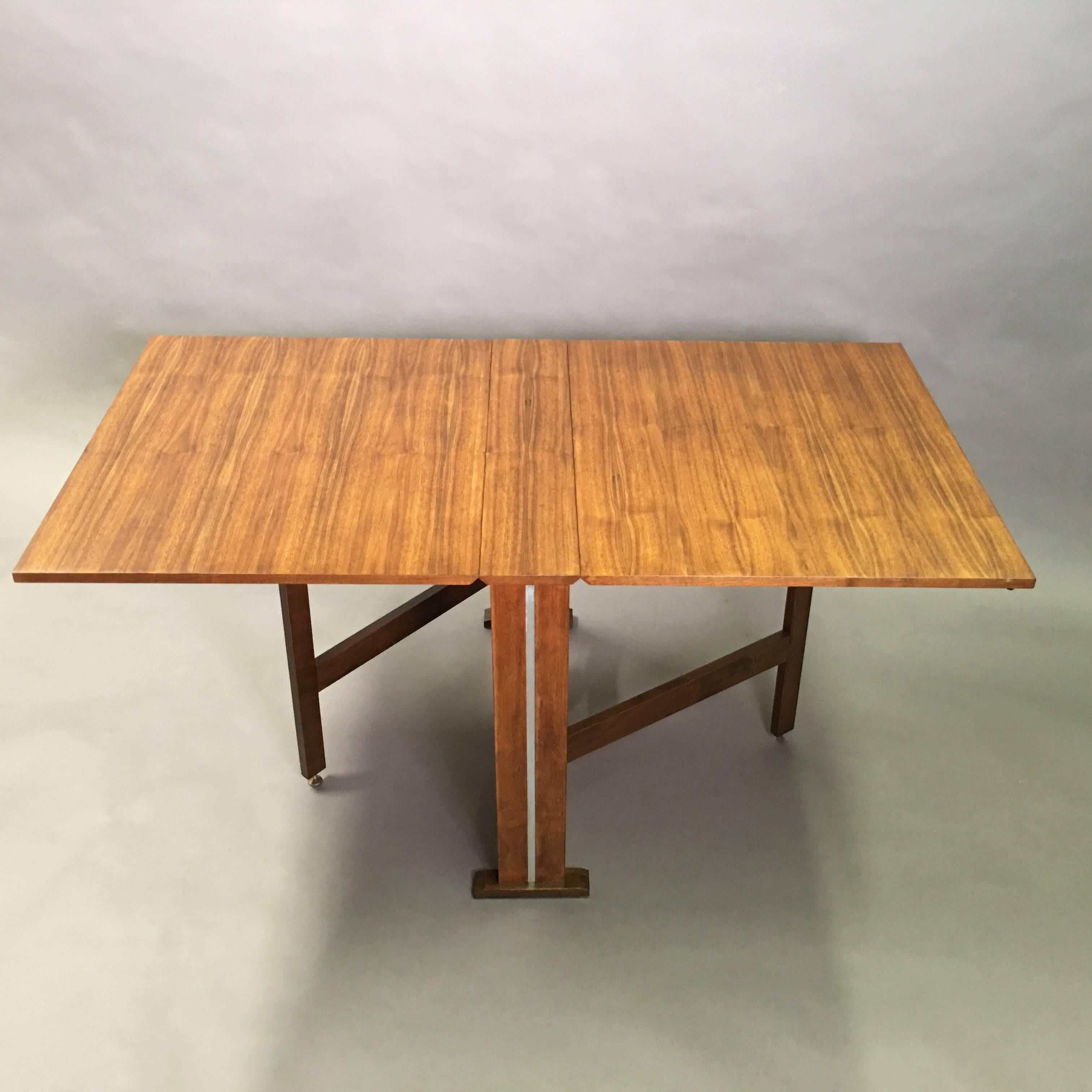 Stylish, Mid-Century Modern, walnut, drop leaf, gate-leg, folding dining table with aluminum trim detail, can be tucked away, used with one leaf up or fully extended to seat 6 people comfortably. The table folds down to be 7.25 in wide. Each leaf is