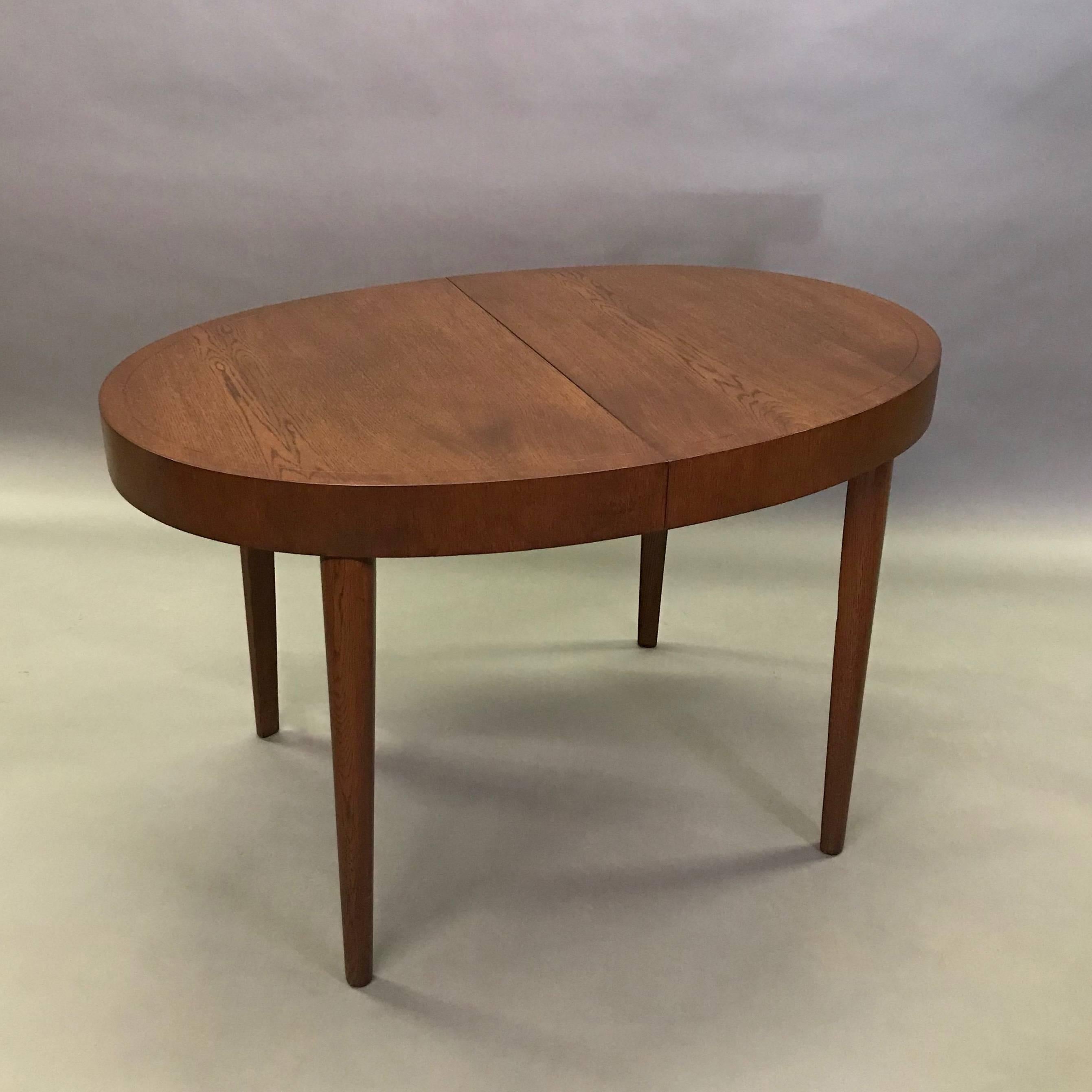 Mid century, oval, walnut stained oak, dining table features a lovely border detail and can extend to accommodate eight people with two 12 inch leaves. The table is 72.25 inches fully extended.