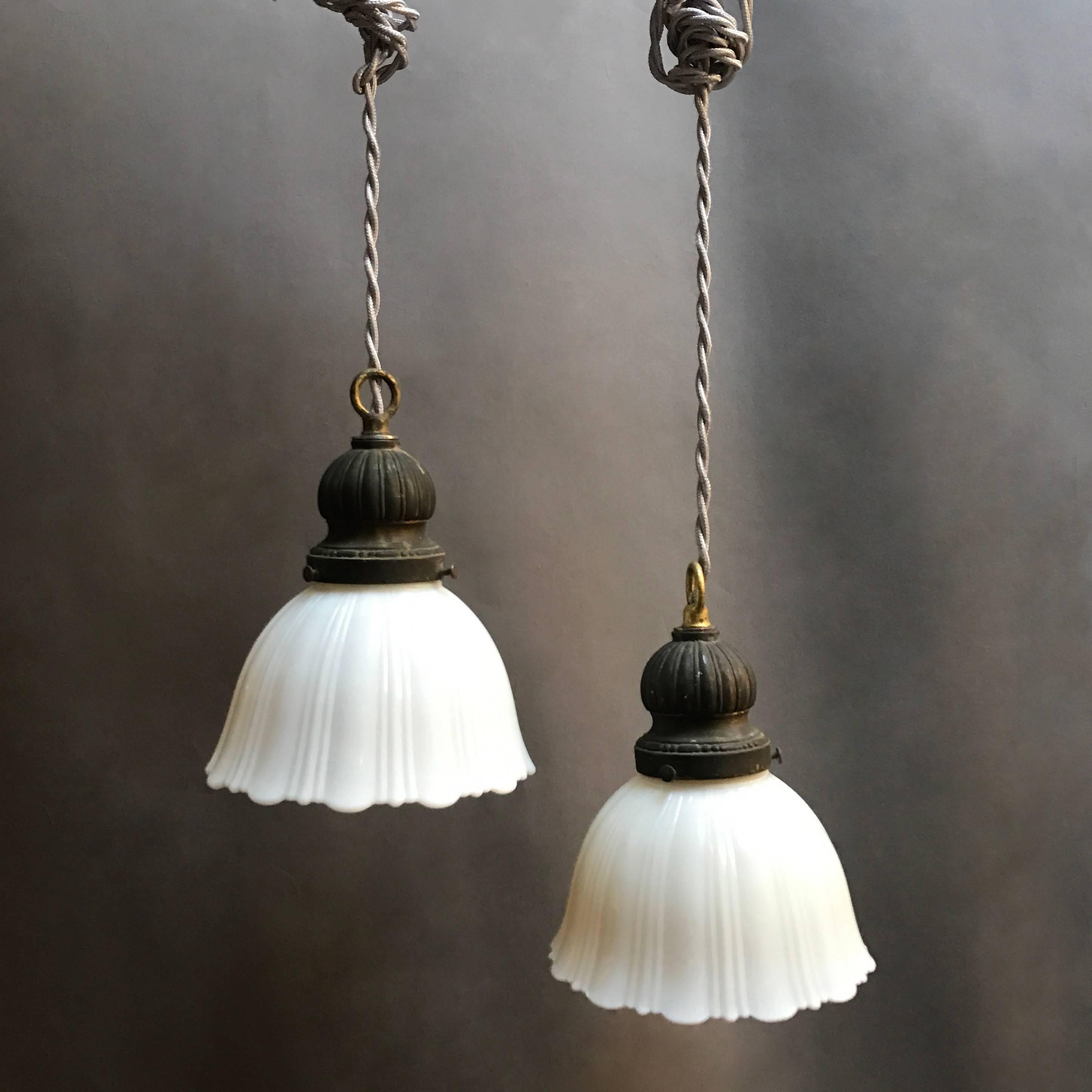 Pair of early 20th century, pendant lights feature fluted milk glass shades with scalloped detail and wonderfully patinated steel fitters are newly wired with 36 inches of gray braided cloth cord to accept up to 200 watts each.