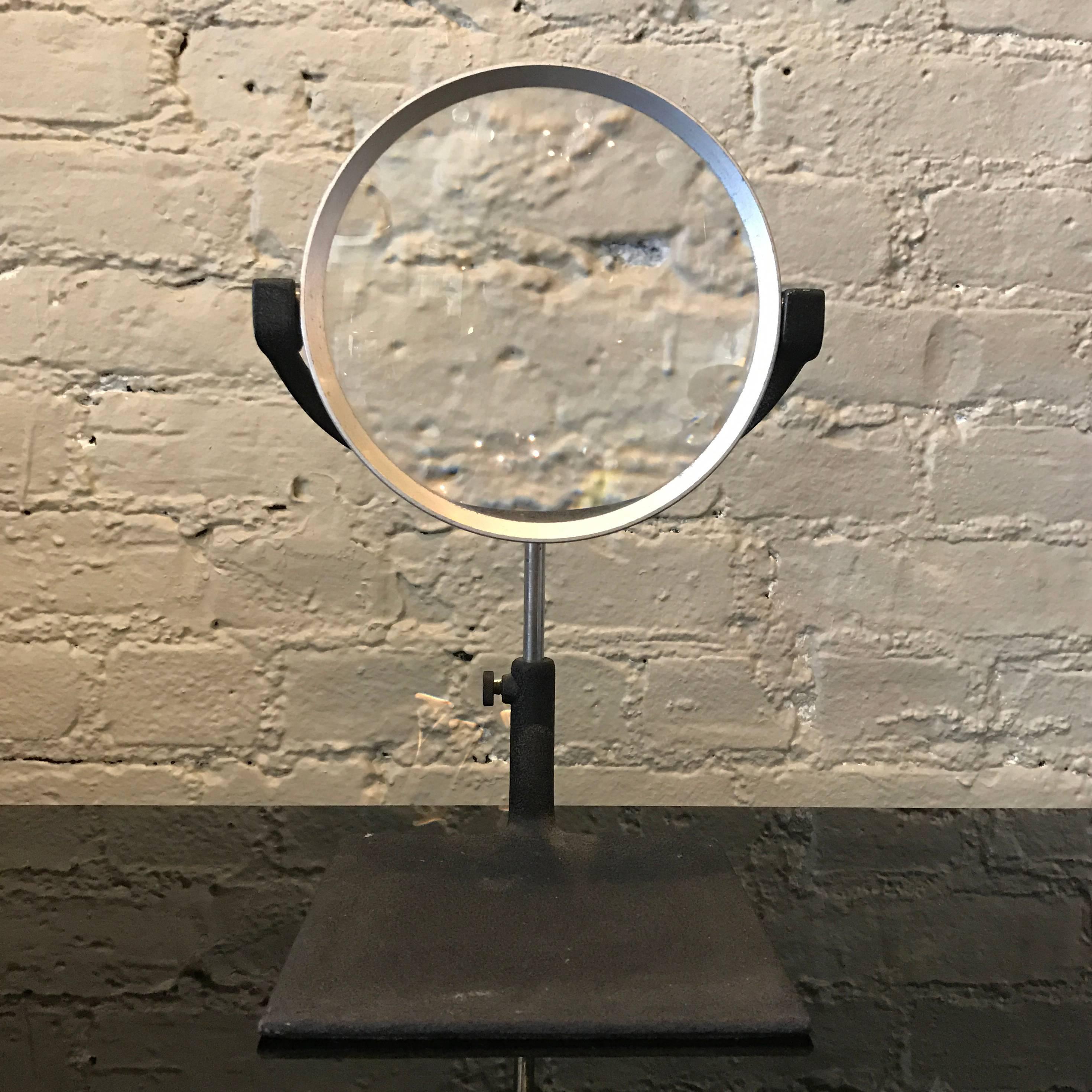 Industrial, 1940s, tabletop magnifying glass by B.M. Levoy Inc., New York City features a square, shrink paint, iron base that the round, aluminum frame magnifying glass rests in. The glass swivels and rotates 360 degrees and is height adjustable