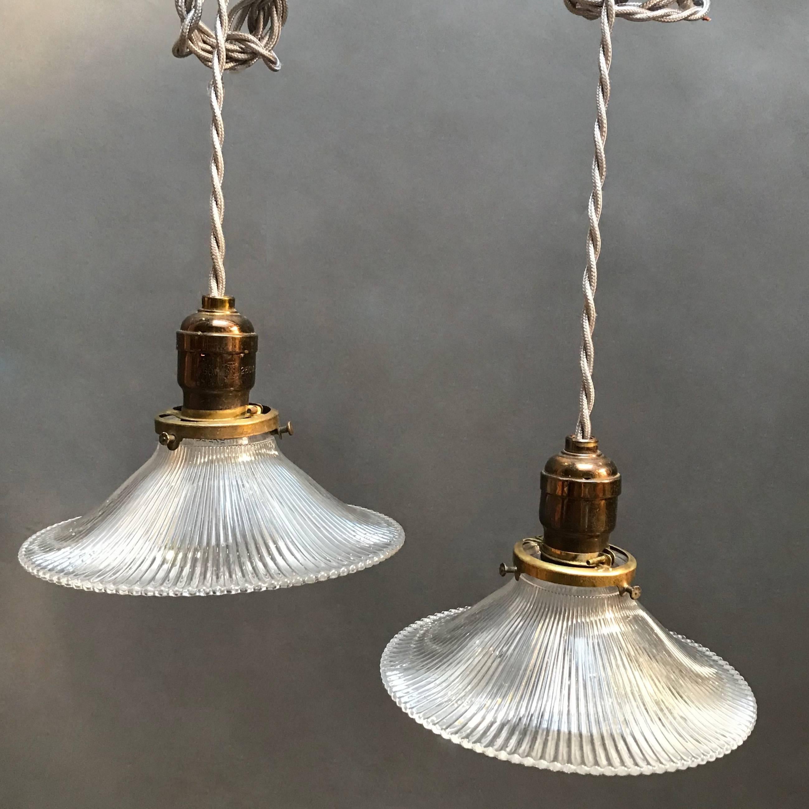 Industrial, early 20th century, Holophane glass pendant lights feature prismatic, fluted shades that slope elegantly from their brass fitters are newly wired for 200 watts with 48 in. of braided cloth cord.