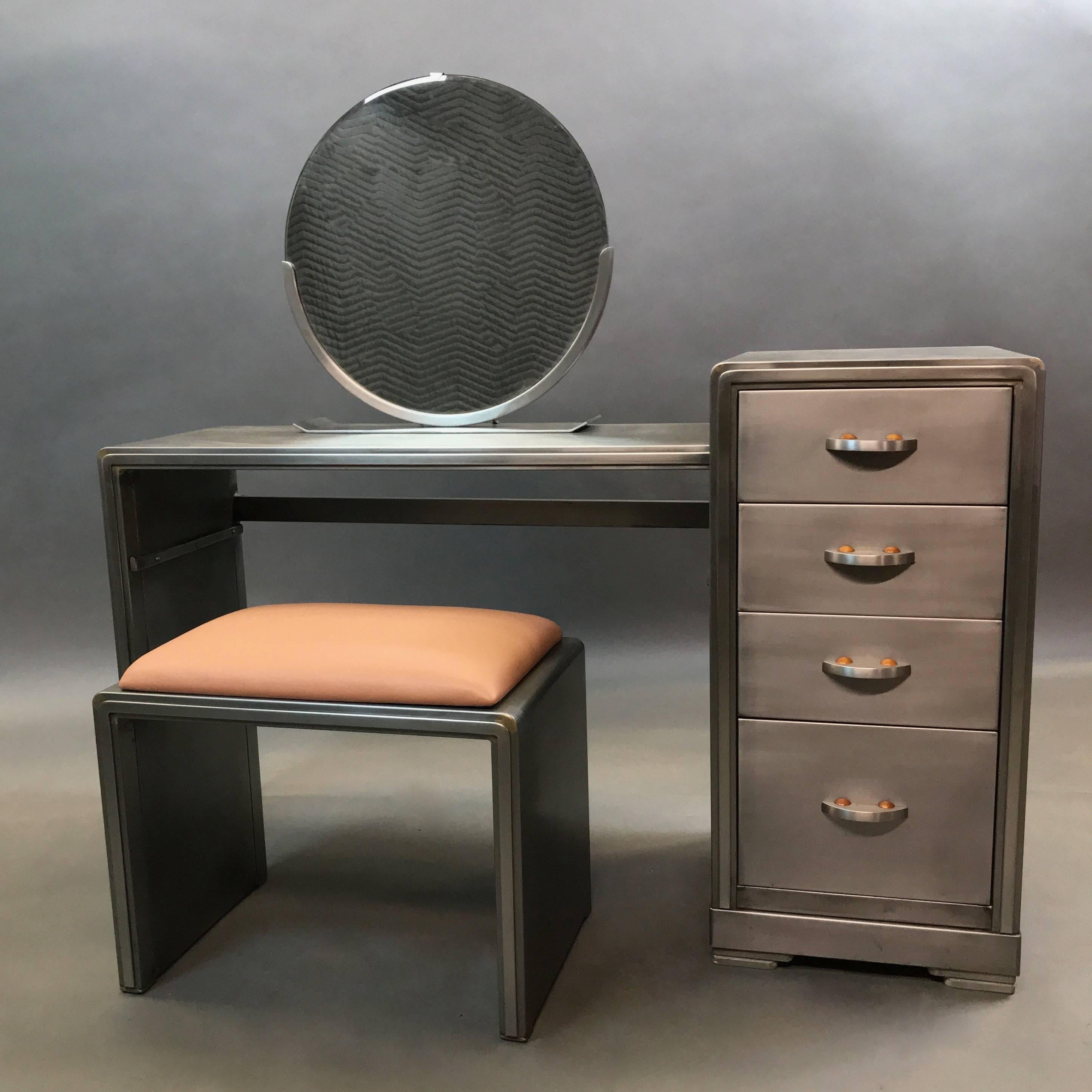 Machine Age, Art Deco, brushed steel vanity desk set designed by Norman Bel Geddes for Simmons Company Furniture features a round, mounted mirror, four-drawer single pedestal with copper detailed pulls and matching bench upholstered in a copper
