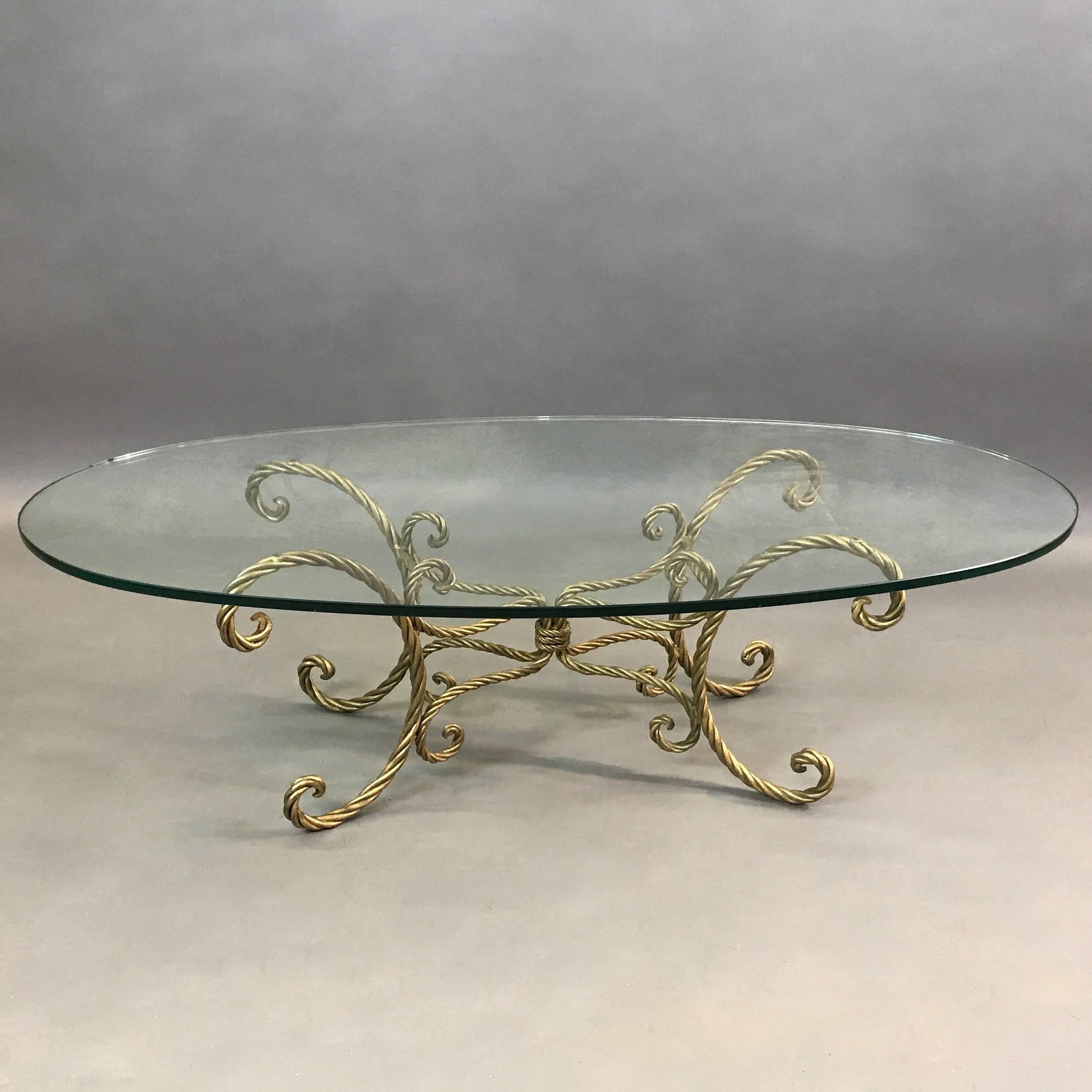 Italian, midcentury, Hollywood Regency, coffee or cocktail table features a gilt iron, braided, rope motif base with a thick oval glass top.
