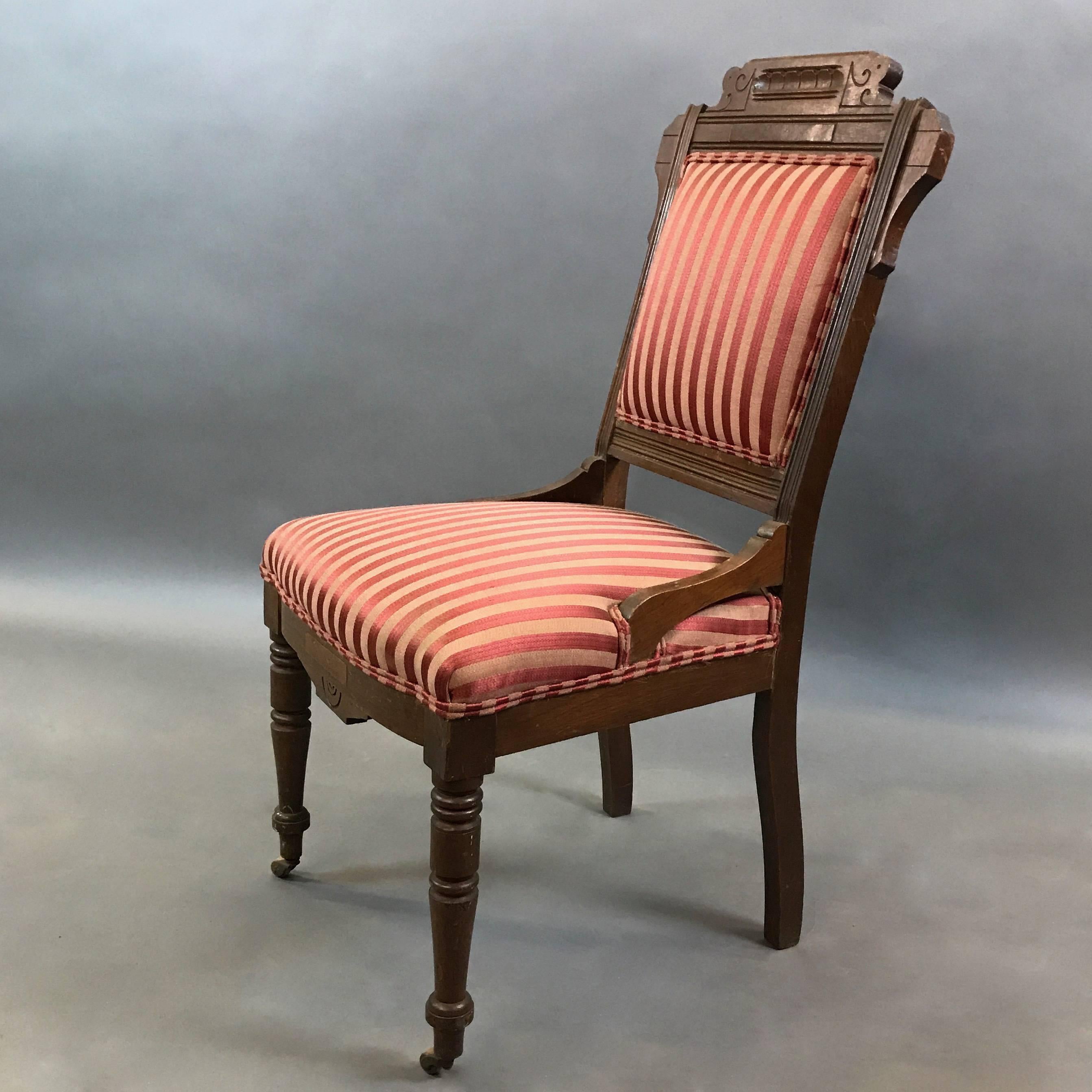 Late 19th century, Eastlake, Victorian, carved mahogany side chair with casters on its front legs features striped silk upholstered seat and back.