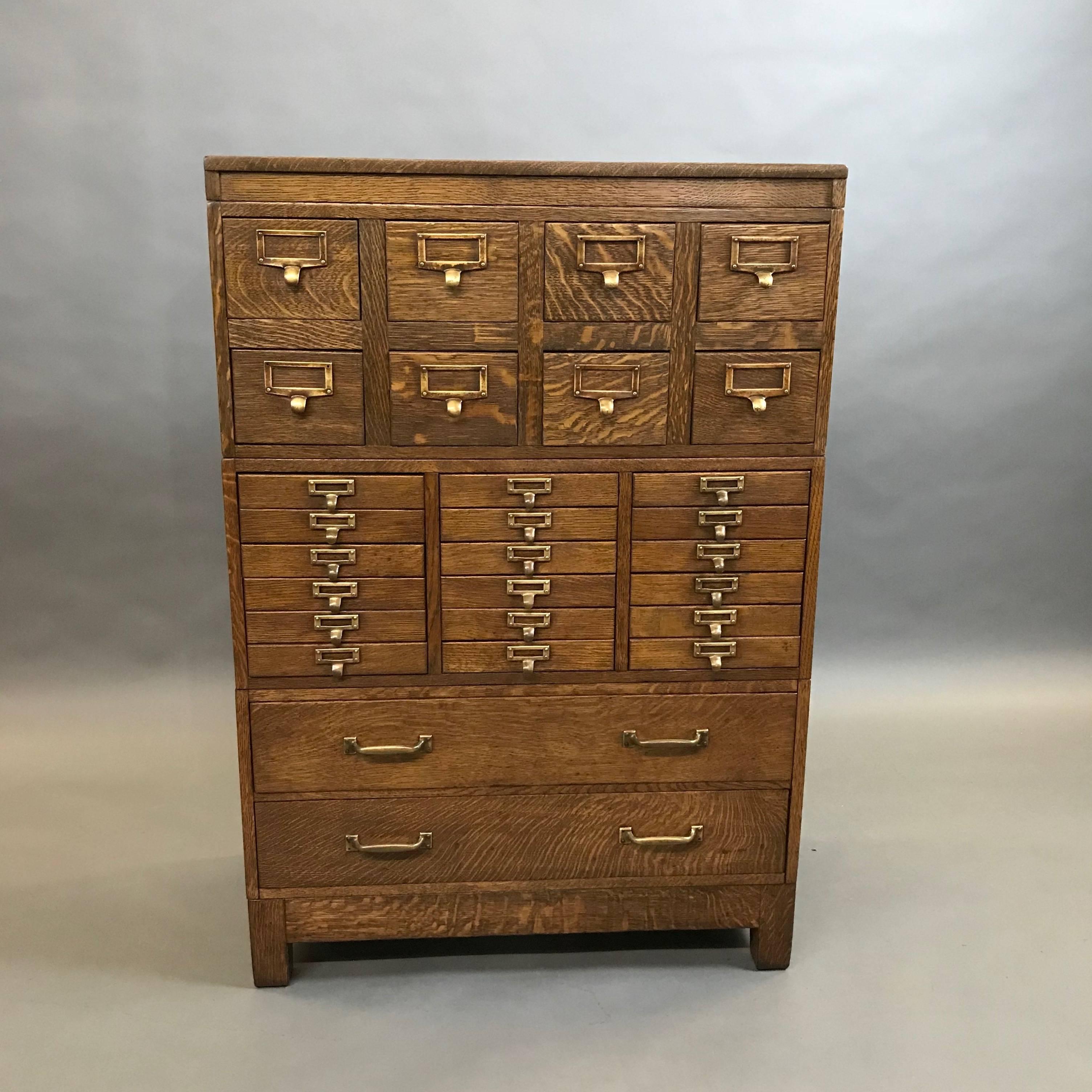 Outstanding, modular, tiger oak office cabinet by Globe Wernicke features 28 drawers in three sizes listed below with brass label frame pulls. The small drawers feature their original green painted interior. The sides have a wonderful panel detail.