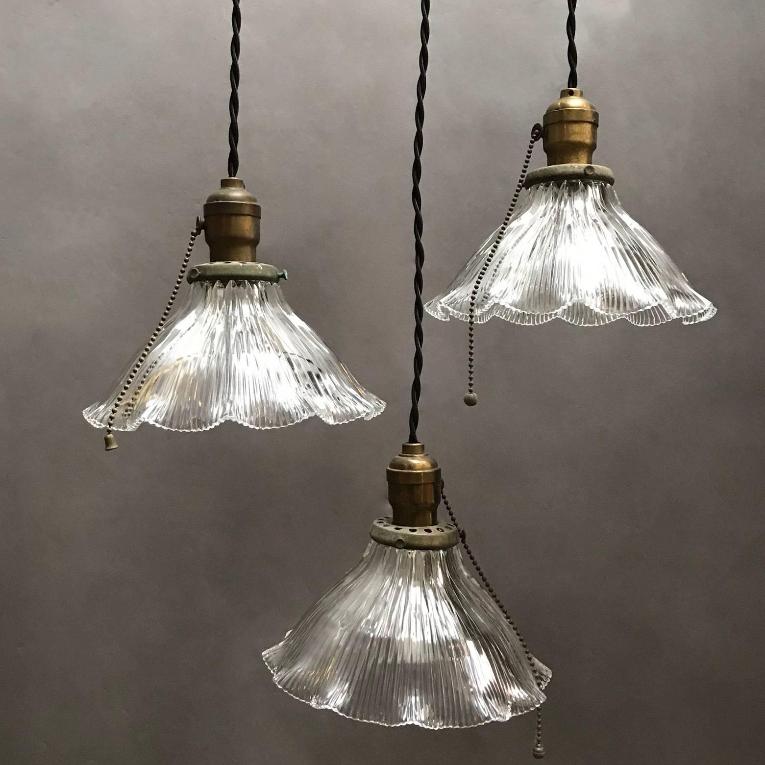 Early 20th century, industrial, Holophane glass pendant lights feature deeply cut, prismatic, wide ruffle, bell-shaped shades with brass fitters and pull chains are newly wired for 200 watts with 48in. of braided cloth cord.