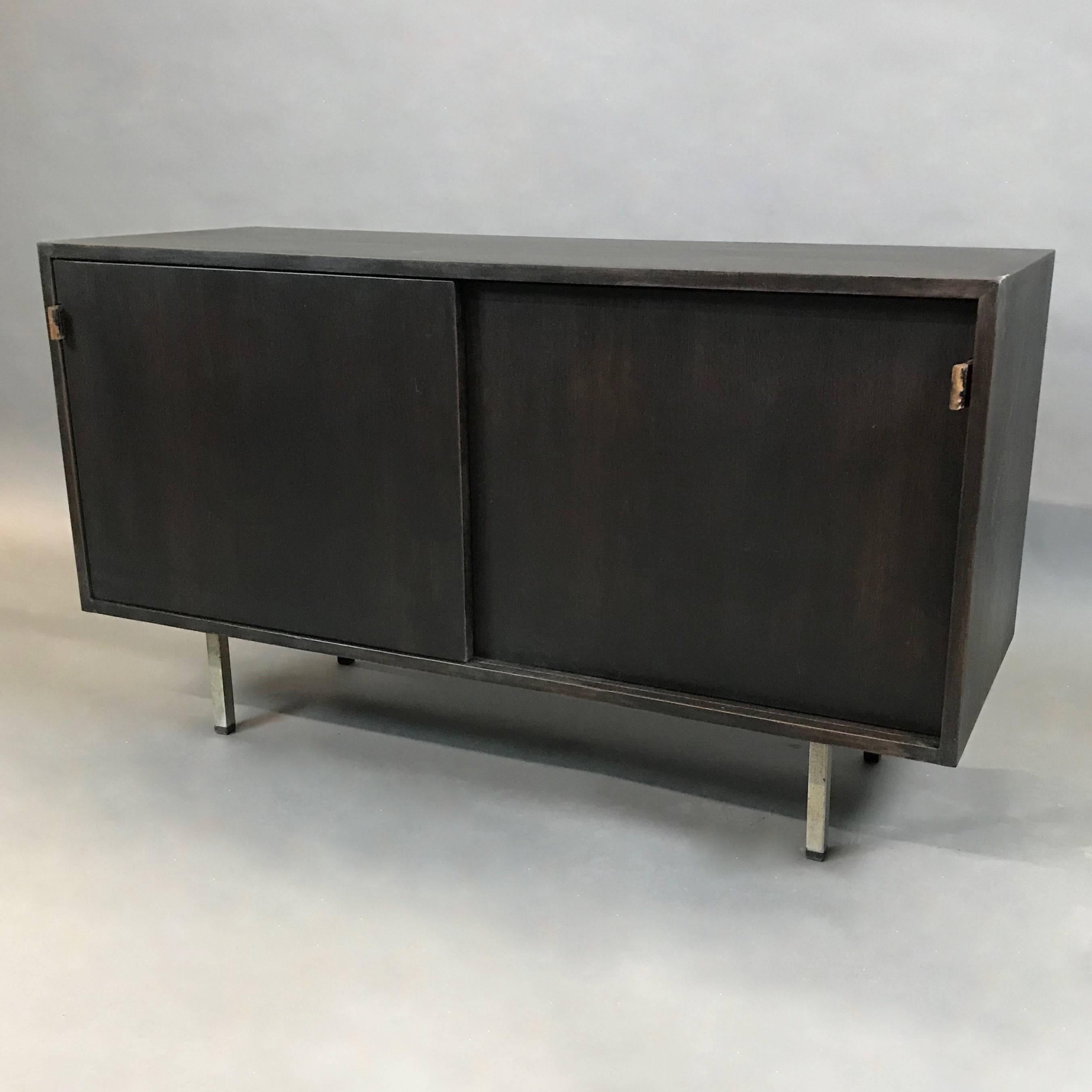 Early credenza or media cabinet by Florence Knoll features an ebonized walnut body, chrome legs, original leather pulls and sectioned interior: 22.75in w / 5.5in w / 16.5in with adjustable and pull out shelves.