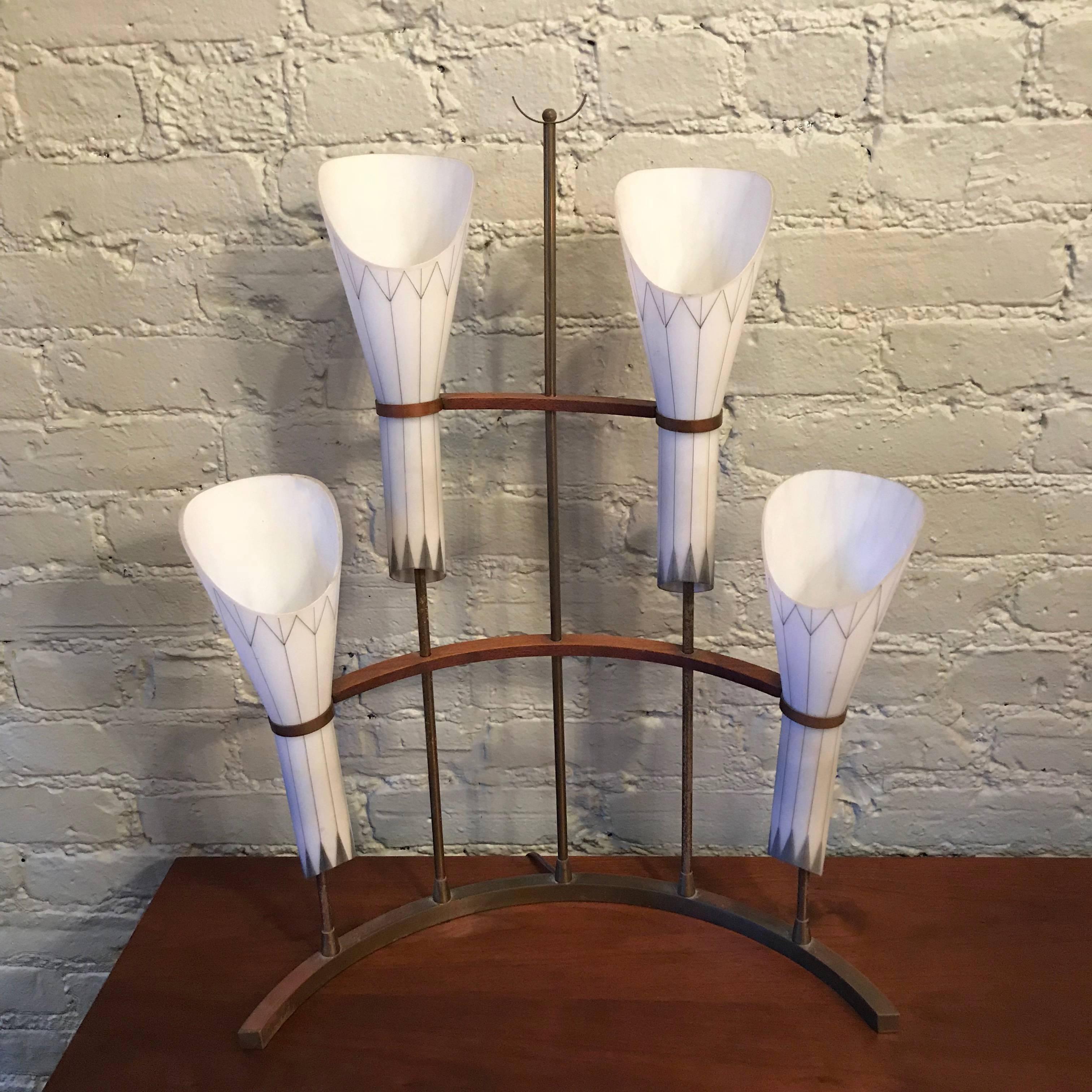 Unusual, Mid-Century Modern, table lamp in the manner of Tommi Parzinger features a crescent shaped base with brass and mahogany stems that house four funnel shaped, frosted white glass with hand-painted gold accent shades. The height to the top of