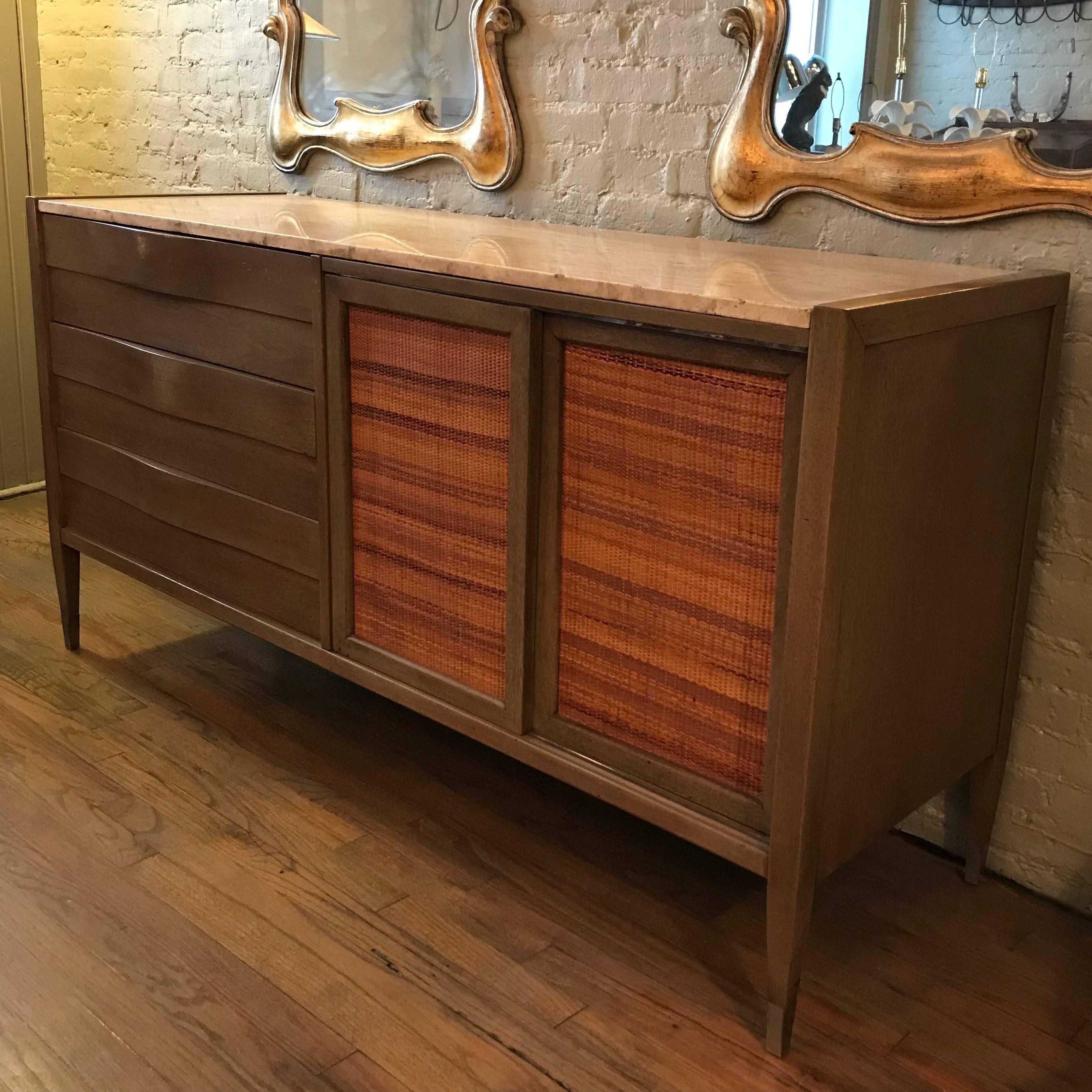 Mid-Century Modern, pickled mahogany credenza or sideboard by American of Martinsville features an Italian travertine top, brass tipped legs, three waved front drawers and woven sliding cabinet doors that open to reveal white lacquered interior
