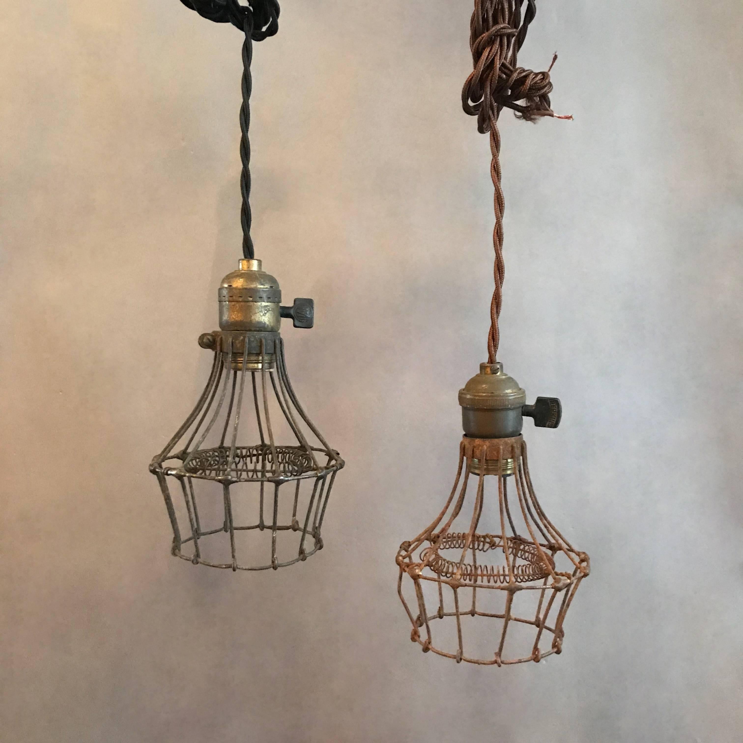 Unusual and rare, 1920s, Industrial, utility, cage pendant lights feature steel wire cages with interior coiled bulb protection and brass fitters with switches. These lights are newly wired to accept up to a 200 watt bulb with 48in. of braided cloth