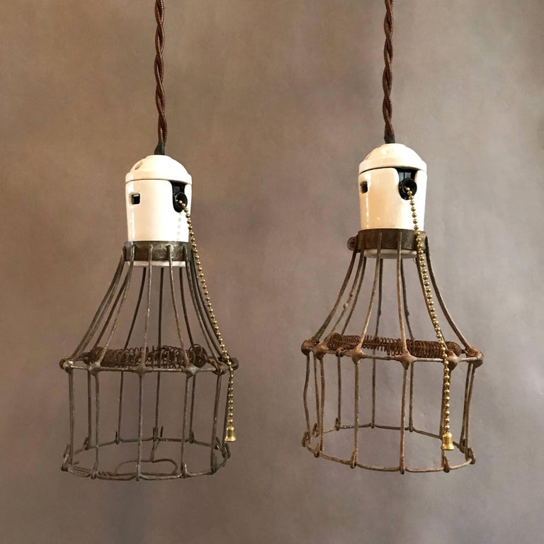 Unusual and rare, 1920s, Industrial, utility, cage pendant lights feature steel wire cages with interior coiled bulb protection and porcelain fitters with switches. These lights are newly wired to accept up to a 200 watt bulb with 48in. of braided