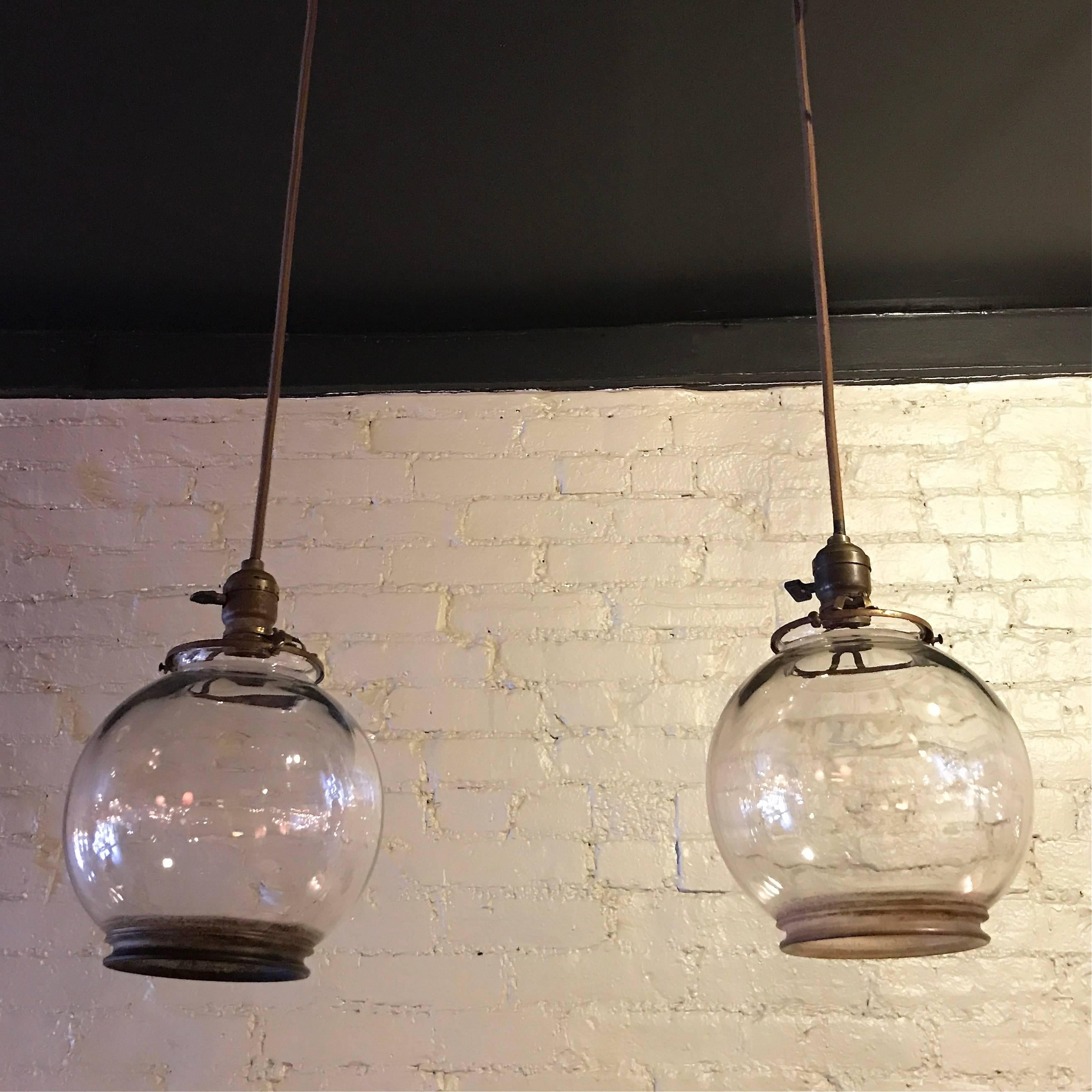 Pair of antique pendant lights featuring converted, clear glass, gaslight shades on patinated brass fitters are newly wired with 36 in of brown cloth cord.