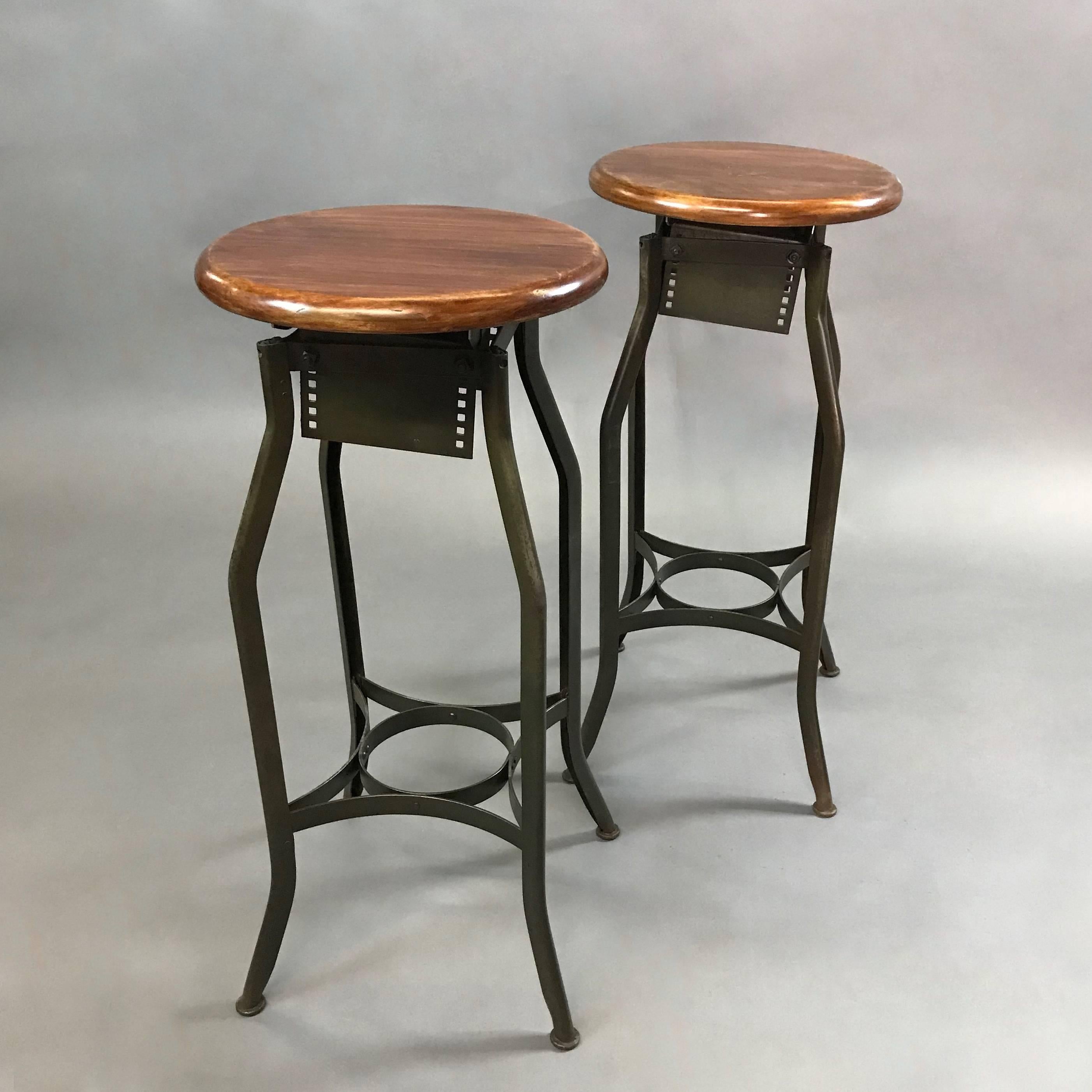 Pair of Industrial shop stool by Toledo Metal Furniture Co. feature stained pine seats and painted steel frames. The seat diameter is 14 inches and the foot print is 20 inches. The stools are height adjustable from 30 - 34 inches by unscrewing the