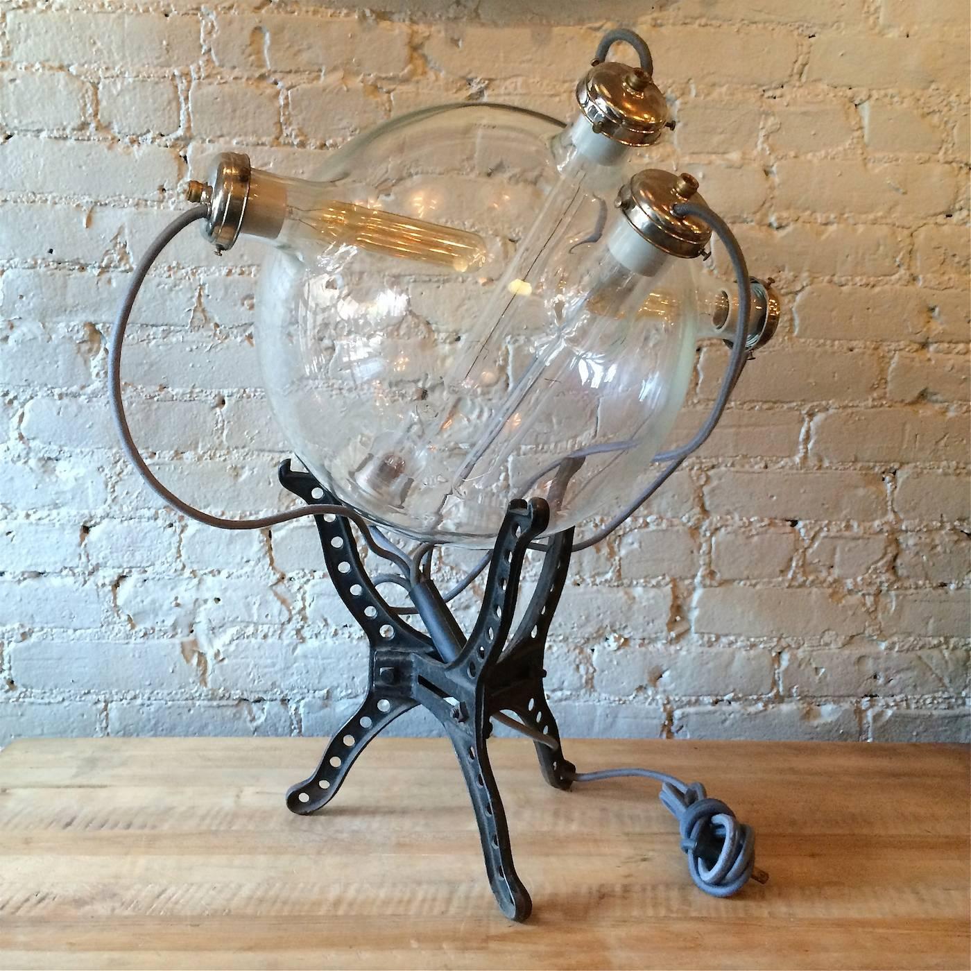 Large-scale, custom, scientific, industrial, sculptural, table lamp with exposed tubular bulbs inside and wiring outside of a large, rare laboratory vessel on a cast iron stand. This lamp is part of the CF Signature Line of custom industrial