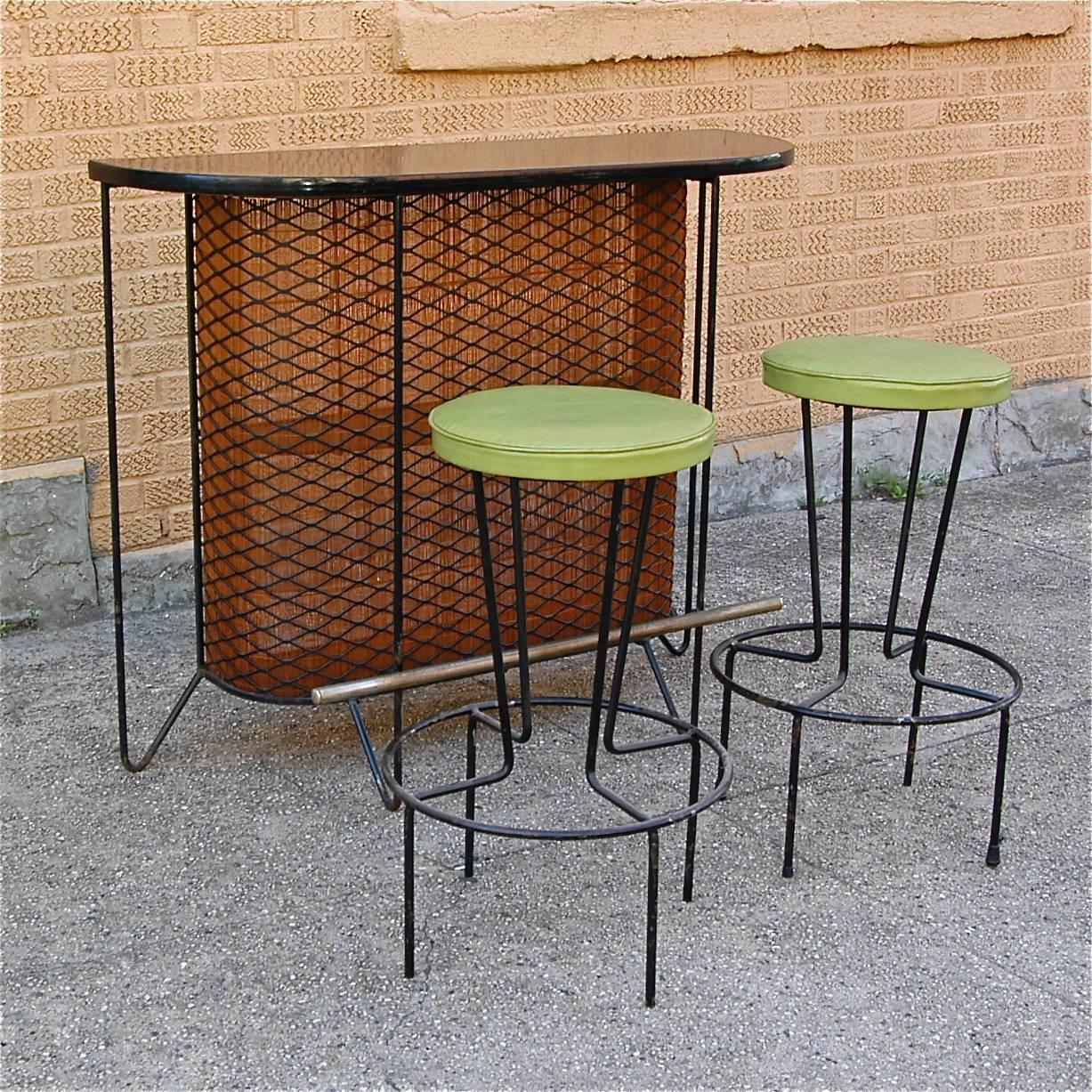 Mid-Century Modern, wrought iron bar set by Frederick Weinberg with black laminate top and woven wood backing has two storage shelves and comes with a pair of matching vinyl upholstered bar stools.

Bar is 39" height x 47" W x 16"