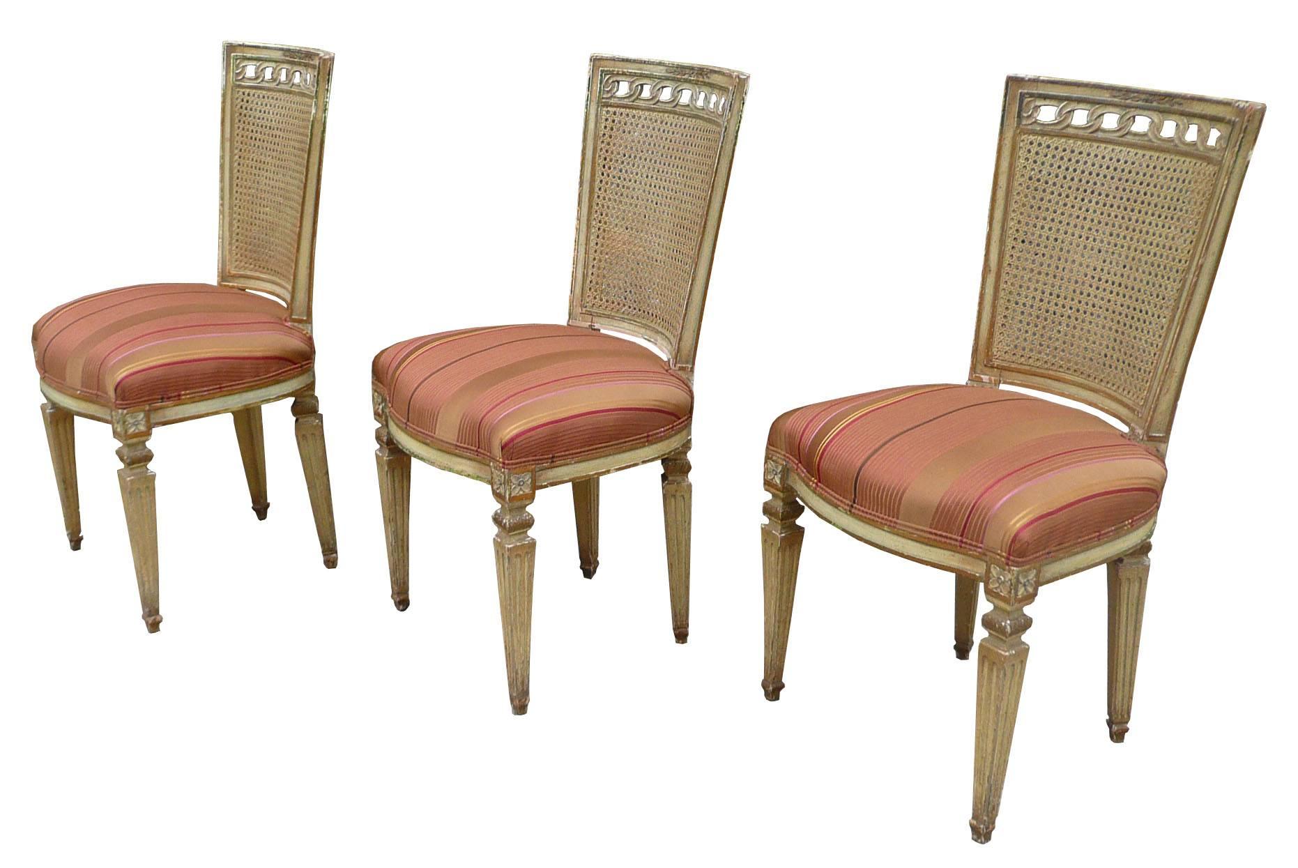Set of three, Louis XVI style, side chairs with cane backs, carved and painted mahogany frames and upholstered seats, circa 1950s. Frames are in original condition and the seats are newly upholstered in a stripped silk.