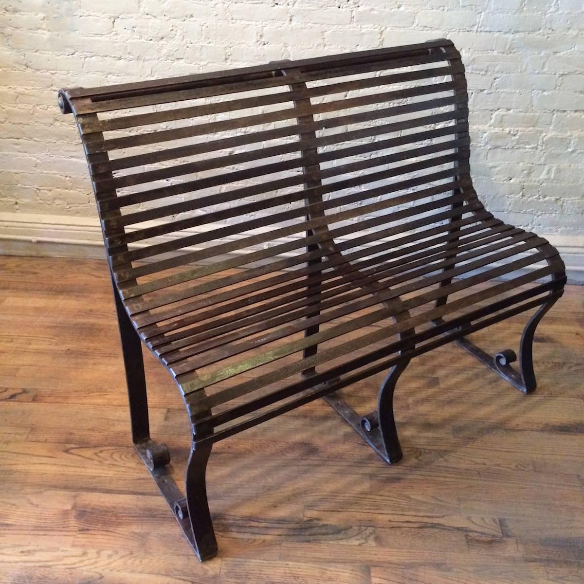 Late 19th century, Victorian park bench is  slatted wrought iron with scrolled accents. The bench bolts to the ground for stability.