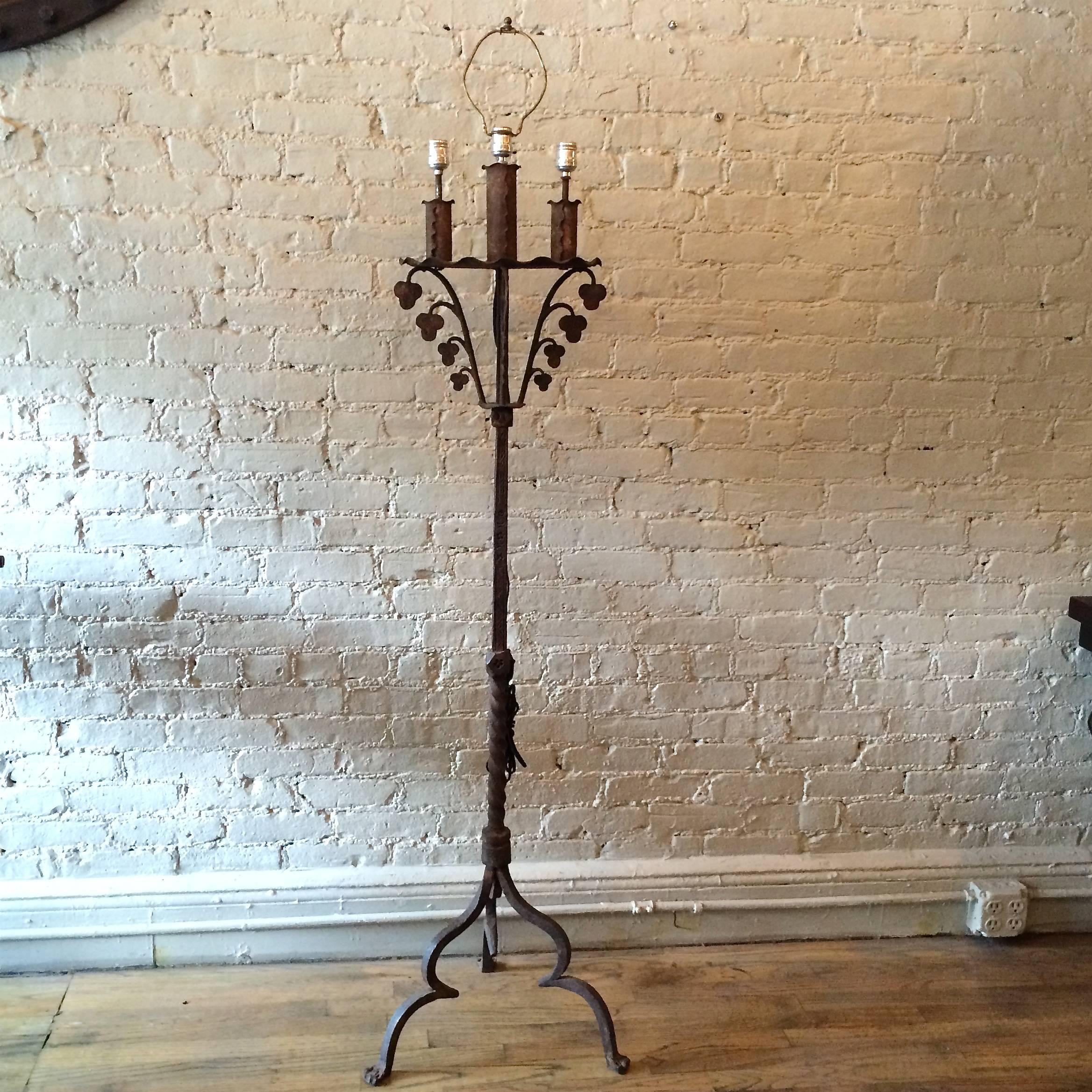 Lampadaire gothique du début du 20e siècle, en fer forgé, de fabrication artisanale, avec une tige décorée de rainures, une base tripode et un sommet feuillagé, avec une armature à trois ampoules dans le style de Samuel Yellin. La lampe est