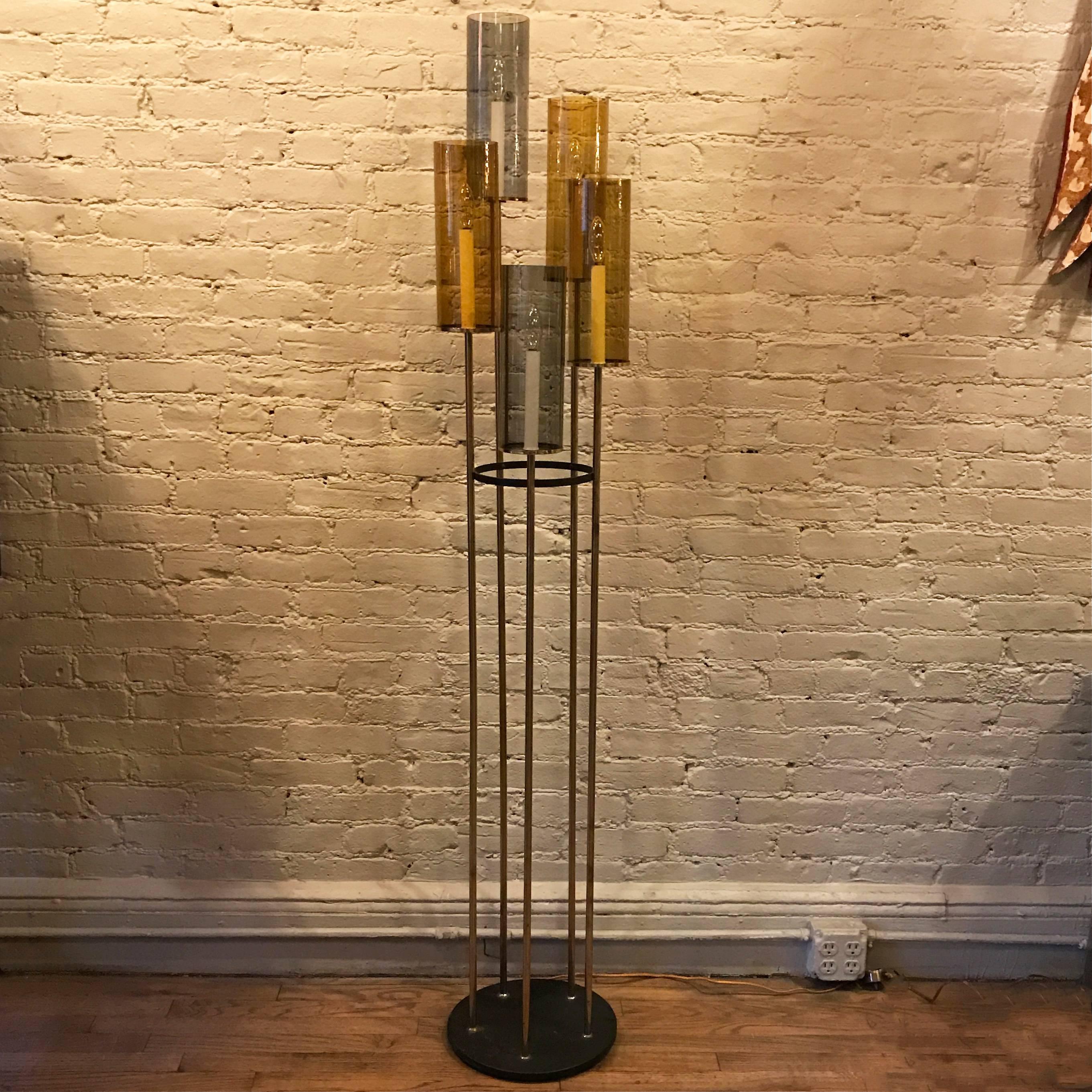 Elegant, Mid-Century Modern floor lamp features five brass stems with cascading candle lights covered in smoked and amber glass shades on a circular metal base. In the style of Lightolier. 