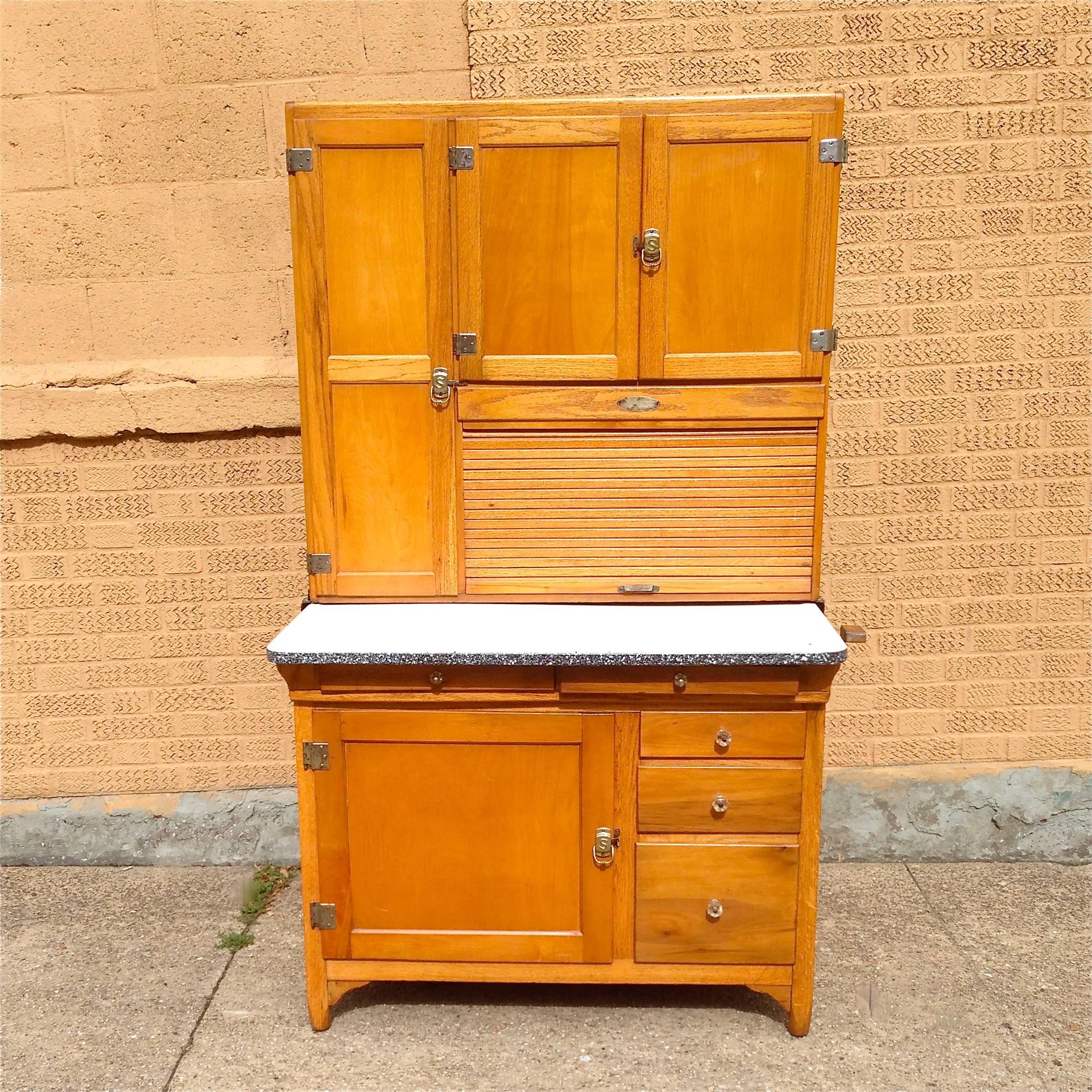 Classic, early 20th century, maple, kitchen hoosier with enamel prep surface, has tons of storage drawers with original glass knobs and roll up, tambour compartment.

Measures: 36" W x 10" top /24" bottom d x 68" ht, prep surface