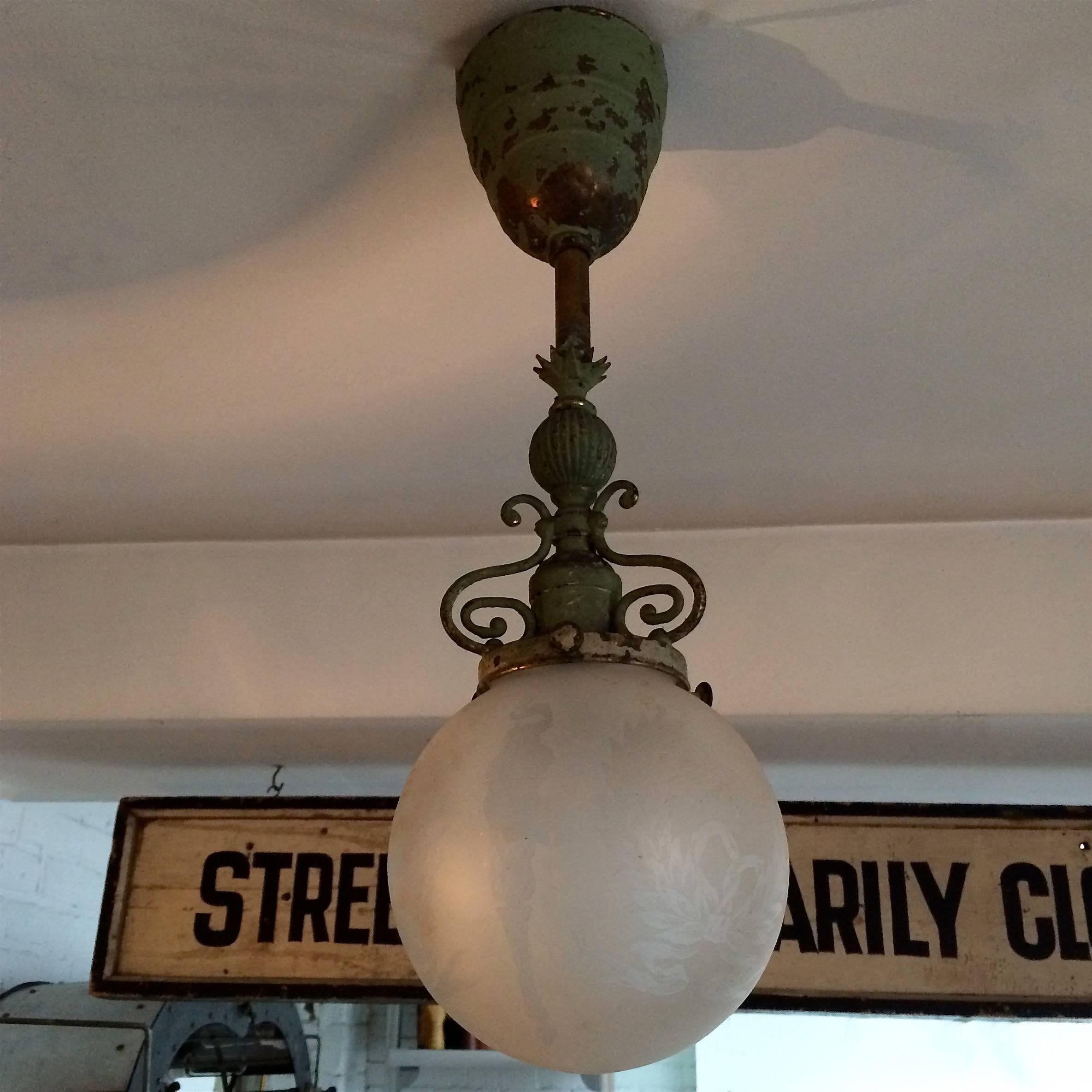 Early 20th century pendant light features an ornate, painted brass pole and canopy with a 6 inch frosted, patterned glass globe shade. The light is wired to accept a 100 watt bulb.