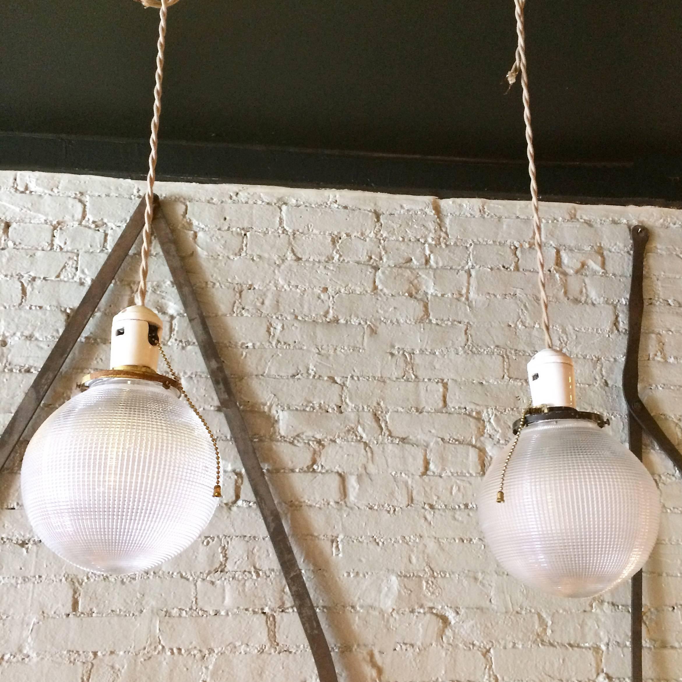 Pair of Industrial, Holophane glass, globe pendant lights feature porcelain sockets with pull chains and brass fitters are newly wired with 52in. of beige braided cord and can accept up to 150 watt bulbs.

The shade is 6.5in. diameter.