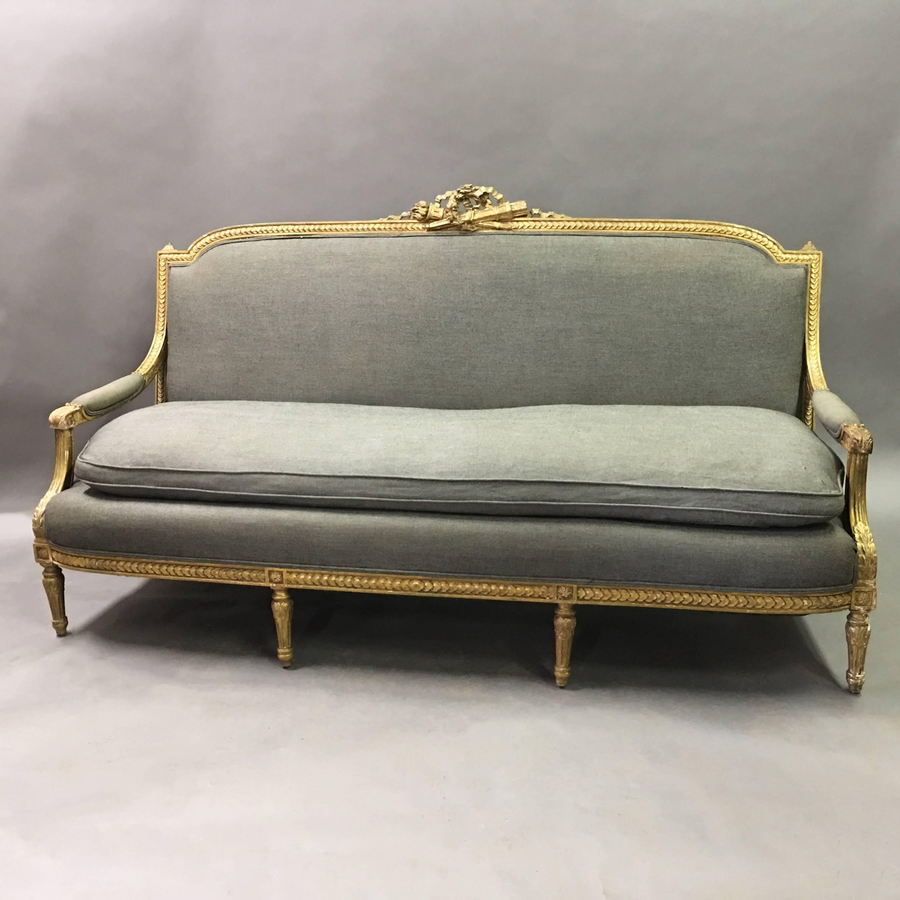 Antique, Louis XVI style, sofa, circa early 1900s features a wonderfully patinated, carved ribbon and wreath motif, giltwood frame with it's original gray wool upholstery.
