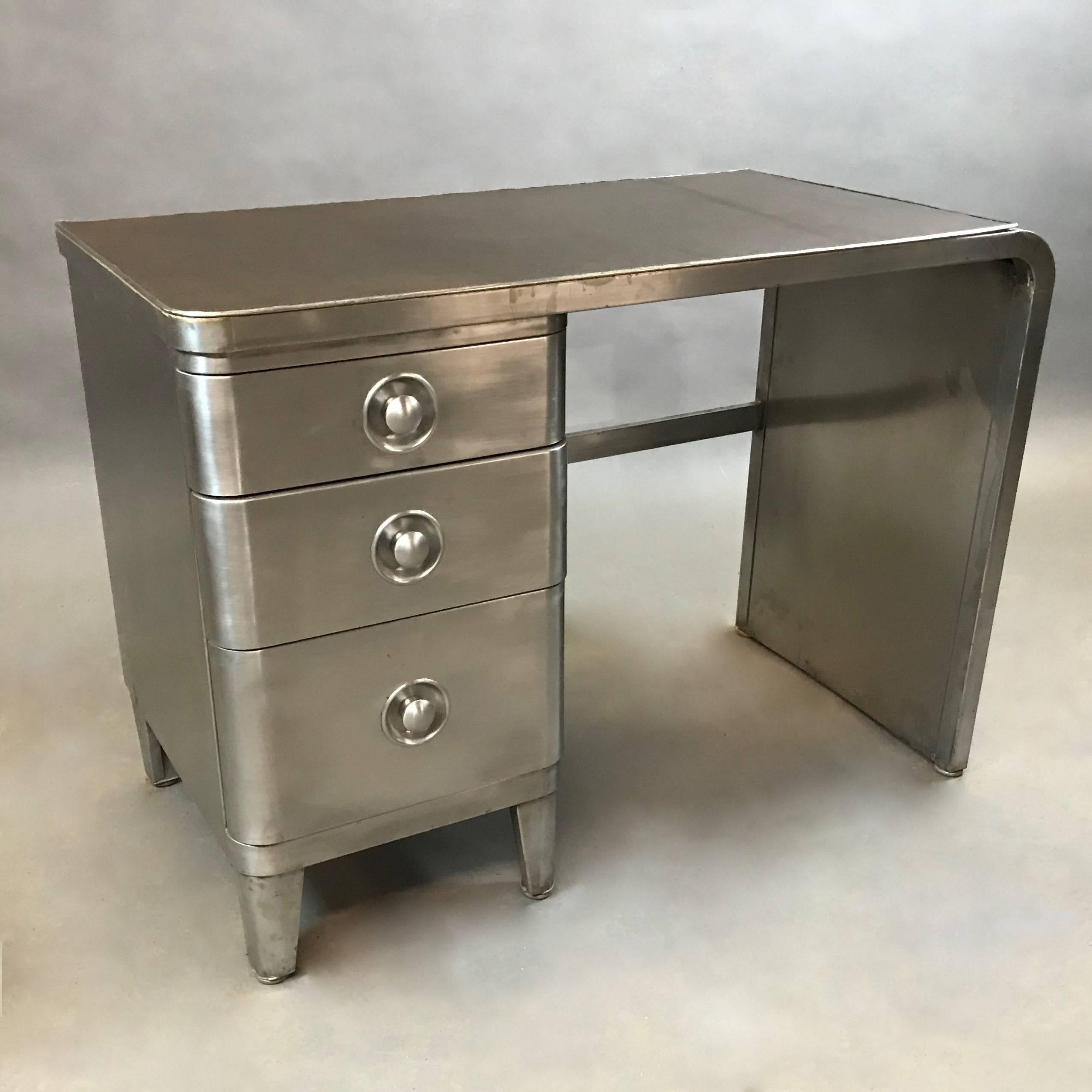 Machine-age, industrial, brushed steel desk by Norman Bel Geddes for Simmons Furniture features three drawers with recessed pulls, waterfall pedestal and custom brown leather top.