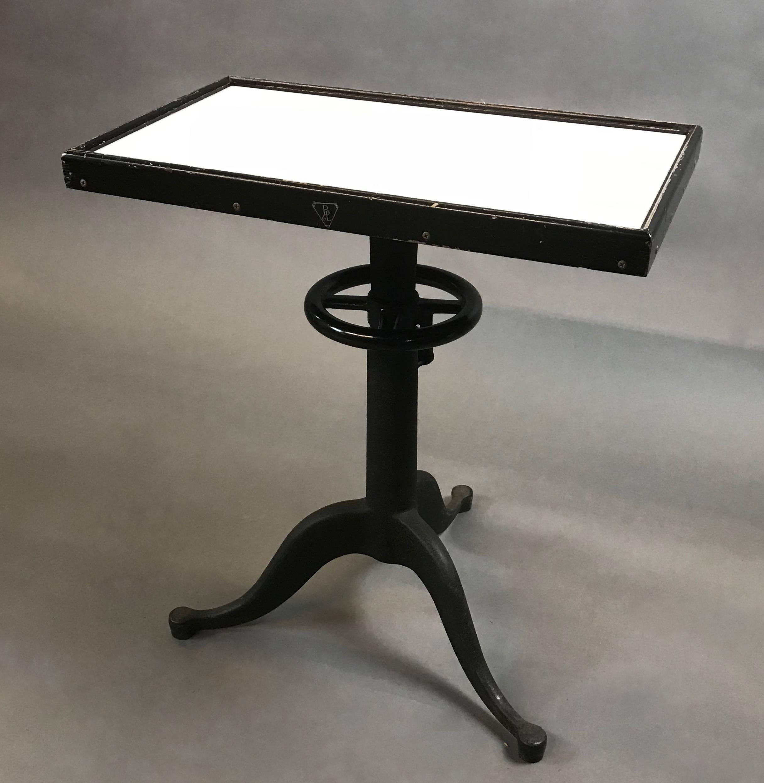 Industrial, optometry examination, table by Bausch & Lomb features a milk glass top in a wood frame atop a height-adjustable, pedestal cast iron and steel base.