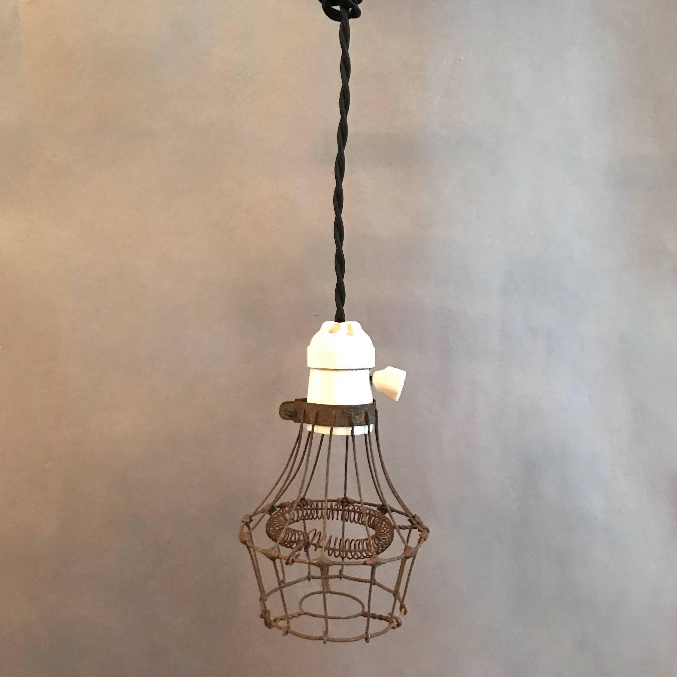Unusual and rare, 1920s, Industrial, utility, cage pendant light features a steel wire cage with interior coiled bulb protection and porcelain fitter with switch. The light is newly wired to accept up to a 200 watt bulb with 48in. of braided cloth