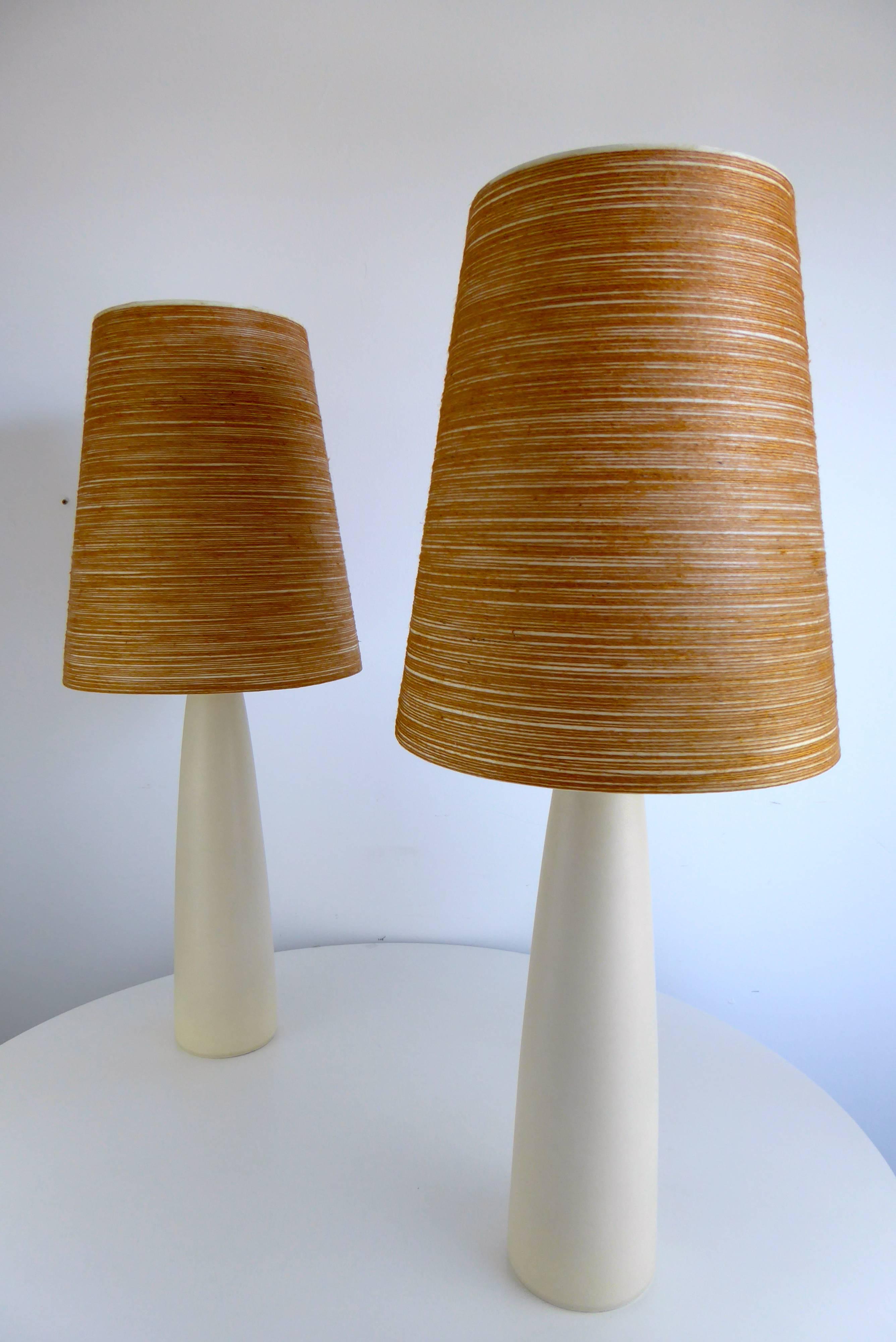 Rare and impressive pair of 1960s Danish modern ceramic bone white glazed table lamps by Lotte and Gunnar Bostlund with original fiberglass shades featuring intricate string detail.

Measures: 34.75 inches to top of finial.
22 inches to top of