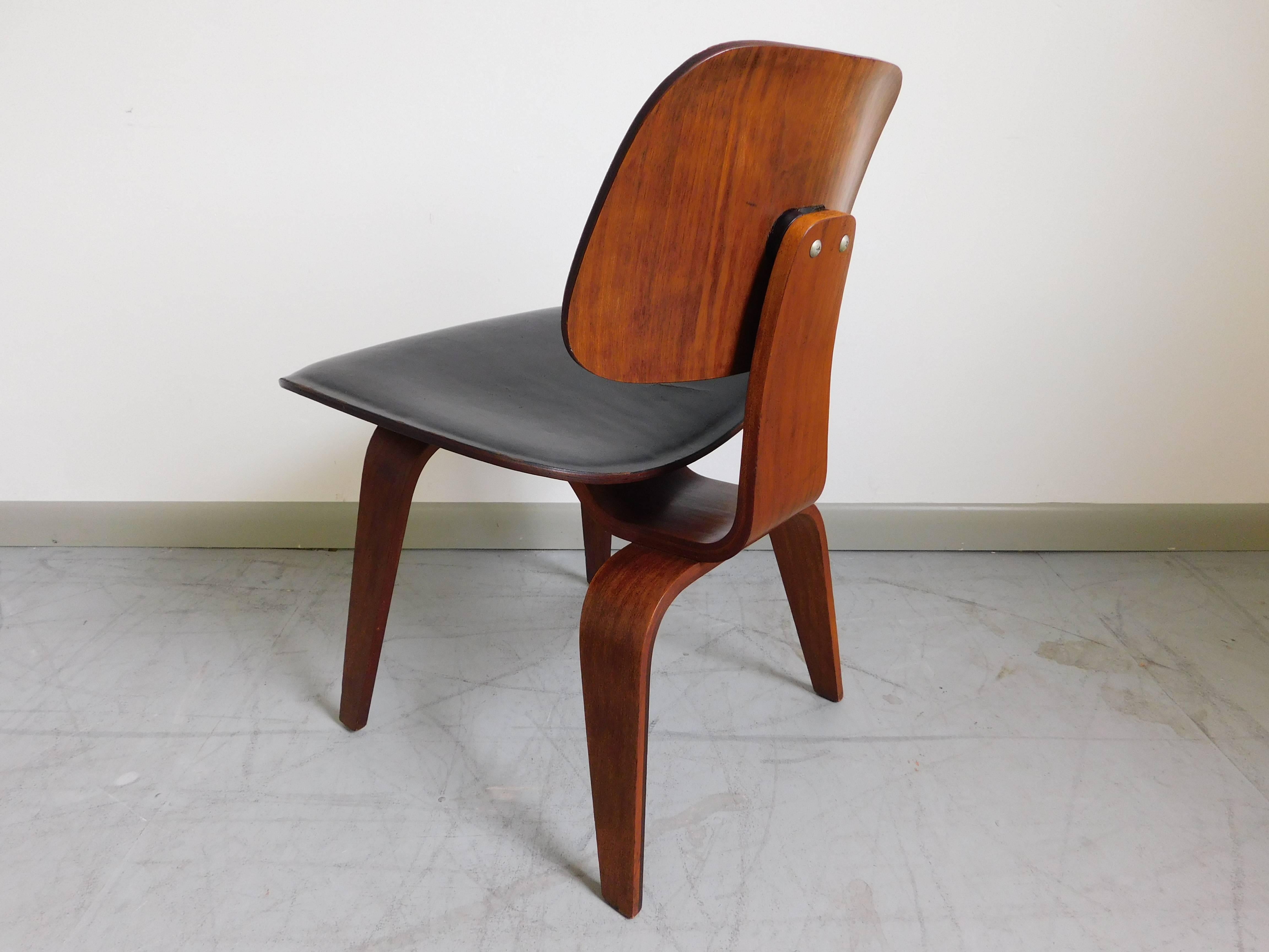 Early custom order DCW chair by Charles and Ray Eames for Herman Miller, 1950s. Walnut construction with original black leather upholstery. Collector's piece. 

Condition: two areas with tears in the leather.  Foam is hardened. Recommend