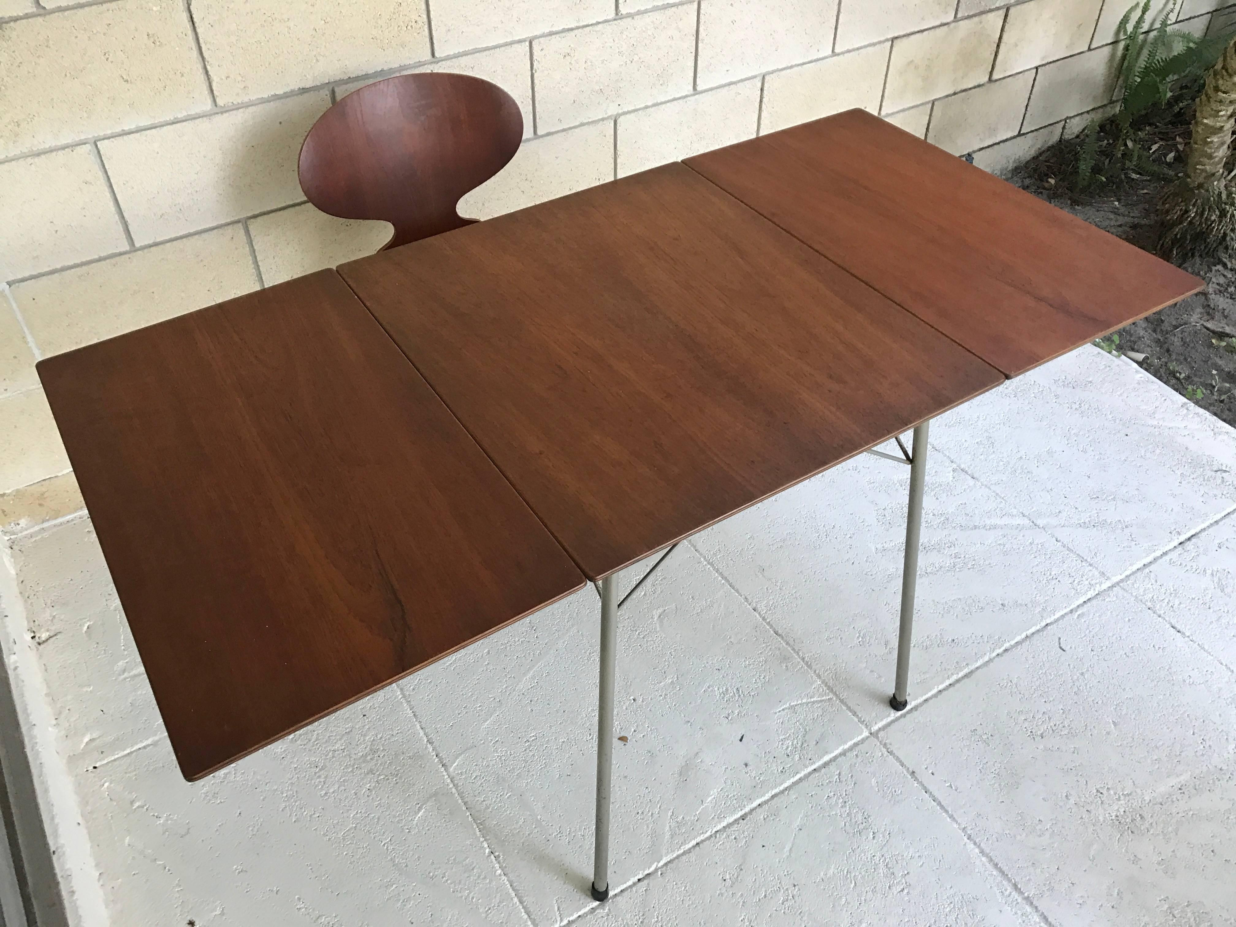 Early petite midcentury Danish Modern drop-leaf dining table in teak designed by Arne Jacobsen for Fritz Hansen, with two early three-leg Ant chairs that came/come with it. The table is perfect for small spaces. The table is in original condition.