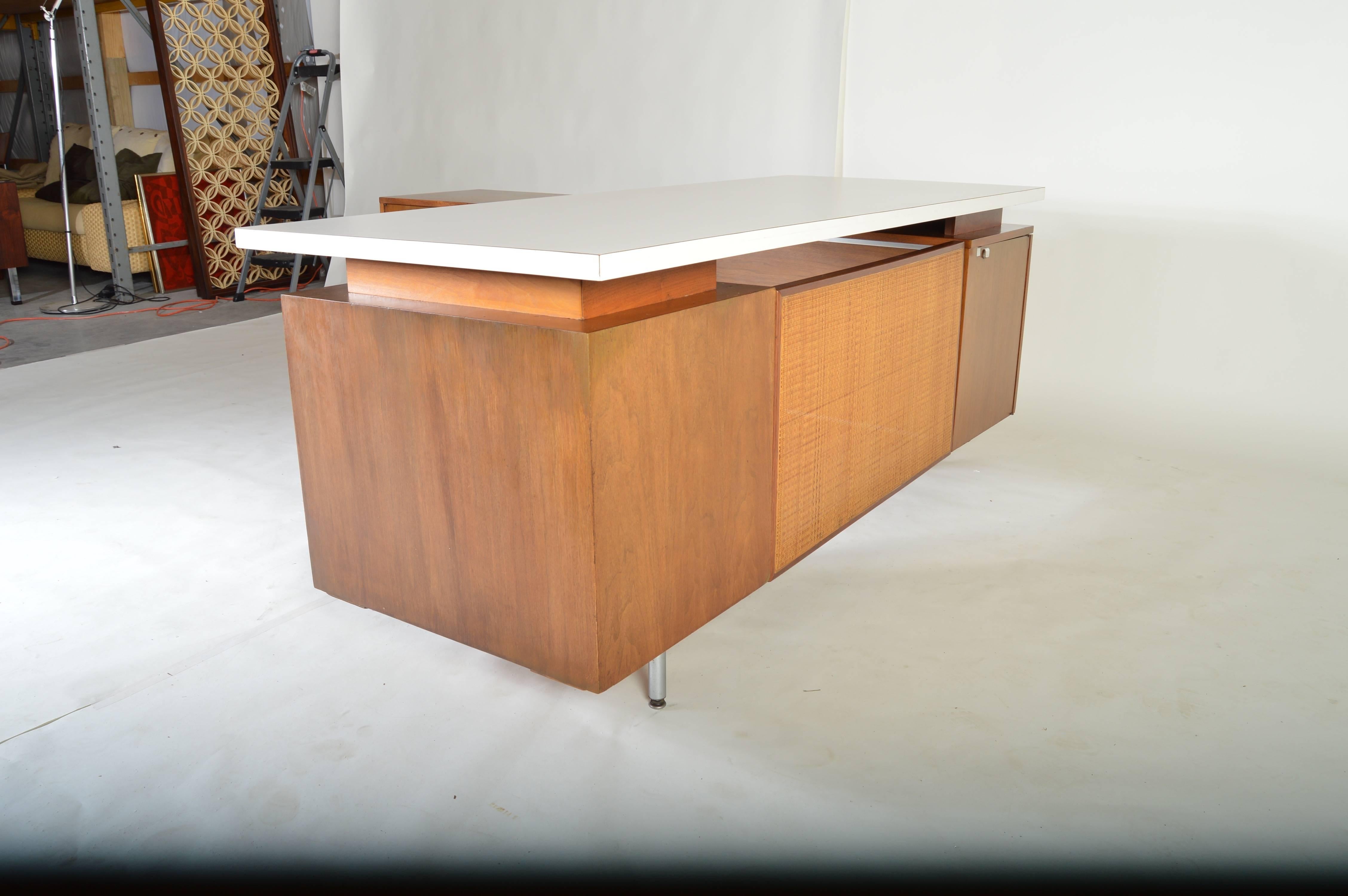 A walnut executive desk designed by George Nelson for Herman Miller having a rare white laminated desk top. 

The desk portion measures: H29.5