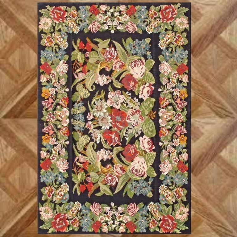 A vintage kilim rug with black field and floral sprays within blossoms border in tones of red, pink and green.