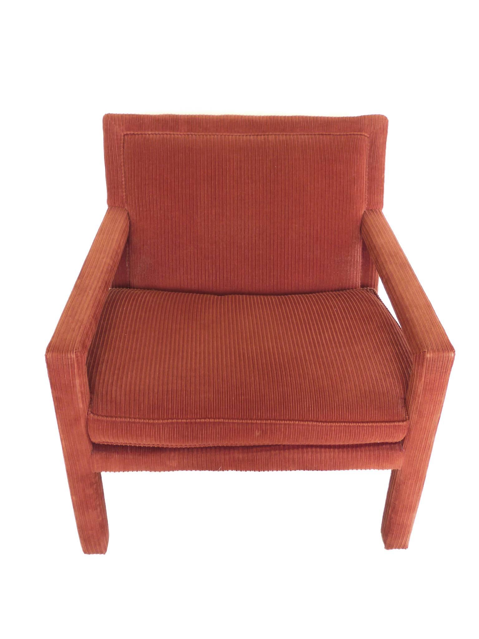 This outstanding pair of armchairs is rich in color and texture. They are completely covered in a carmine-orange corduroy upholstery. Crafted in the manner of Milo Baughman, the chairs are wide with simple, flat planes accentuated by the rich