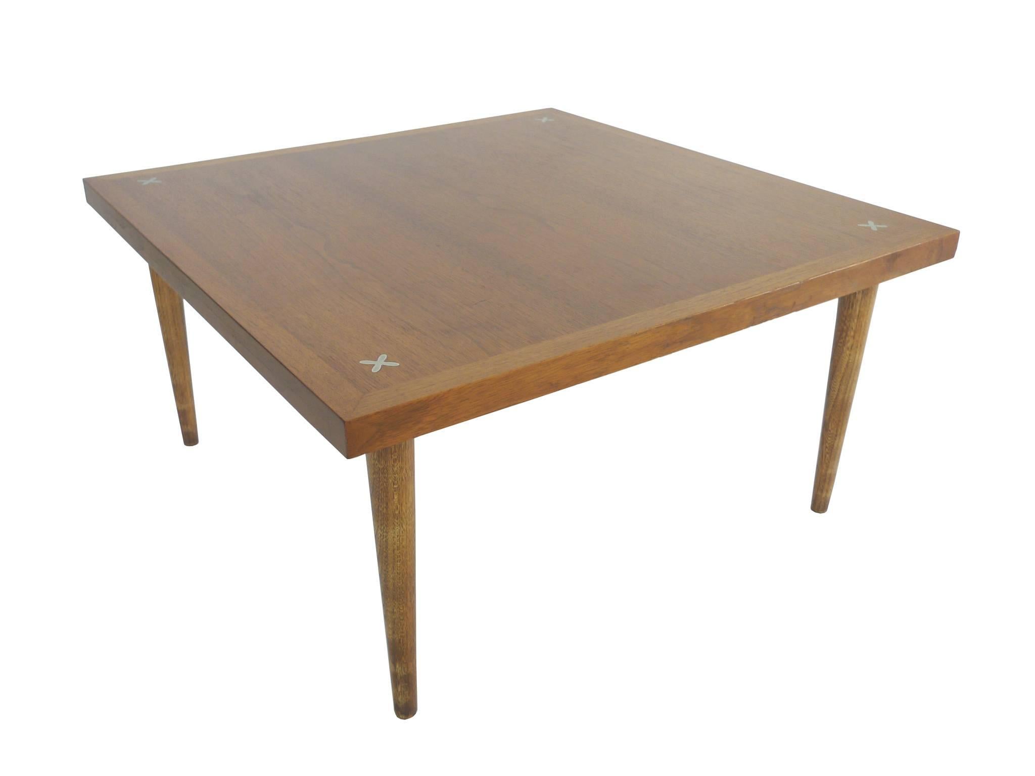 This square walnut cocktail table was designed by Merton Gershun for American of Martinsville. It is newly refinished. Brass X-inlays adorn the tabletop, one at each corner. The legs are high and taper downward. This is an elegant cocktail table,