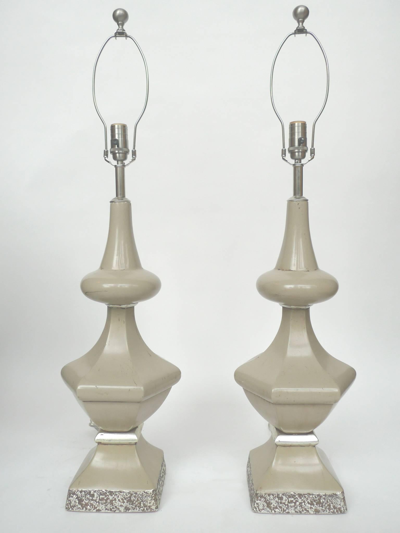 This pair of tall and baluster-shaped table lamps are by the American interior decorator Dorothy Draper. The lamps are comprised of enameled iron with silver-hued details. Included are the original matching shades. The lamps have been rewired with