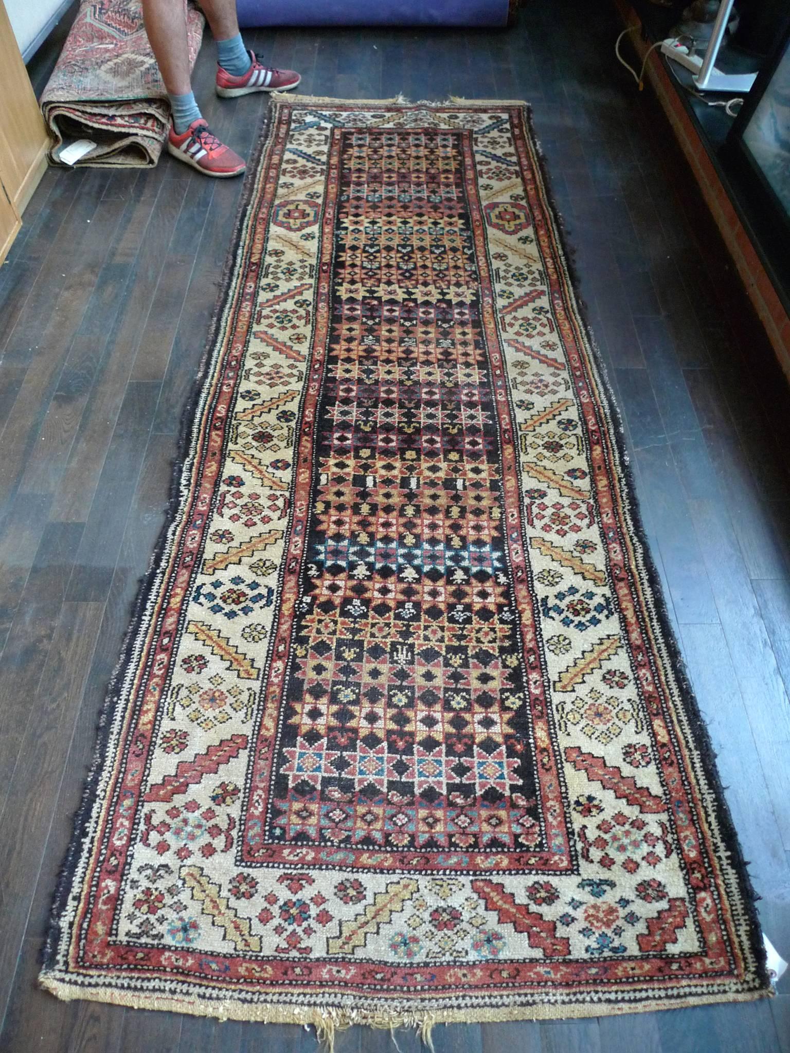 The design of this colorful Turkish runner consists of a central rectangular field in black with star-shaped and geometric forms repeating in columns. The surrounding borders contain other geometric shapes and floral motifs in a pattern of blues,