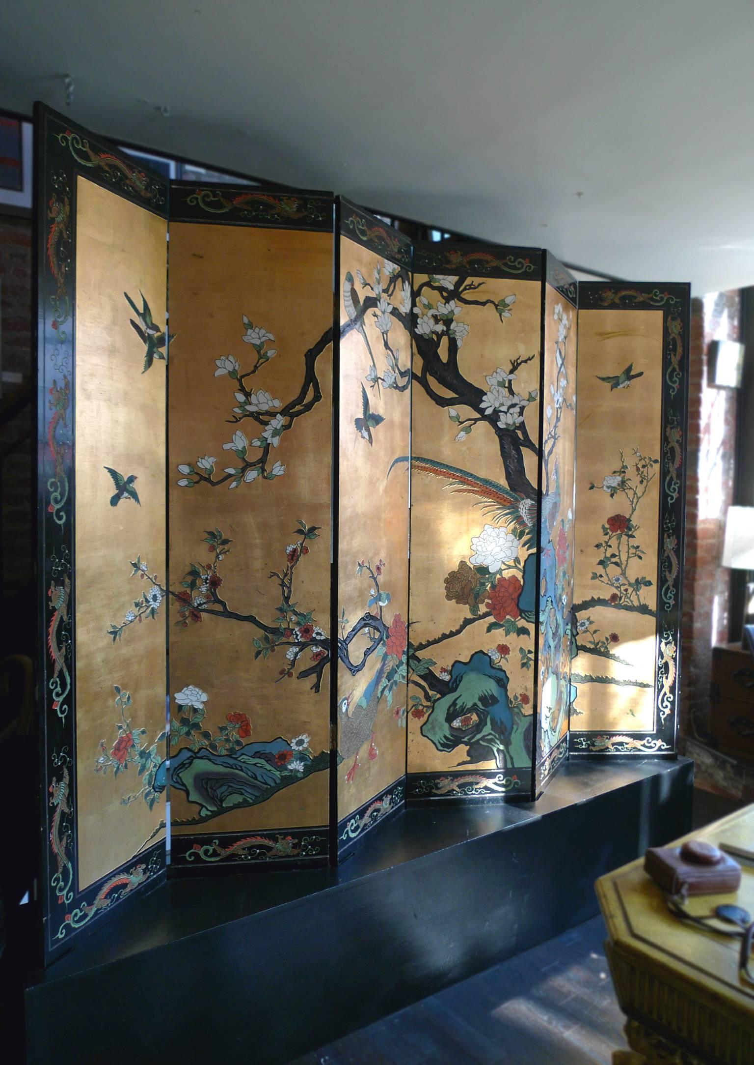 This 20th century Chinese folding screen has two beautifully painted sides. One side portrays a radiant daytime scene rendered in gold-leaf, with gnarled trees and colorful birds that are incised into the panels and painted in. The scene is framed