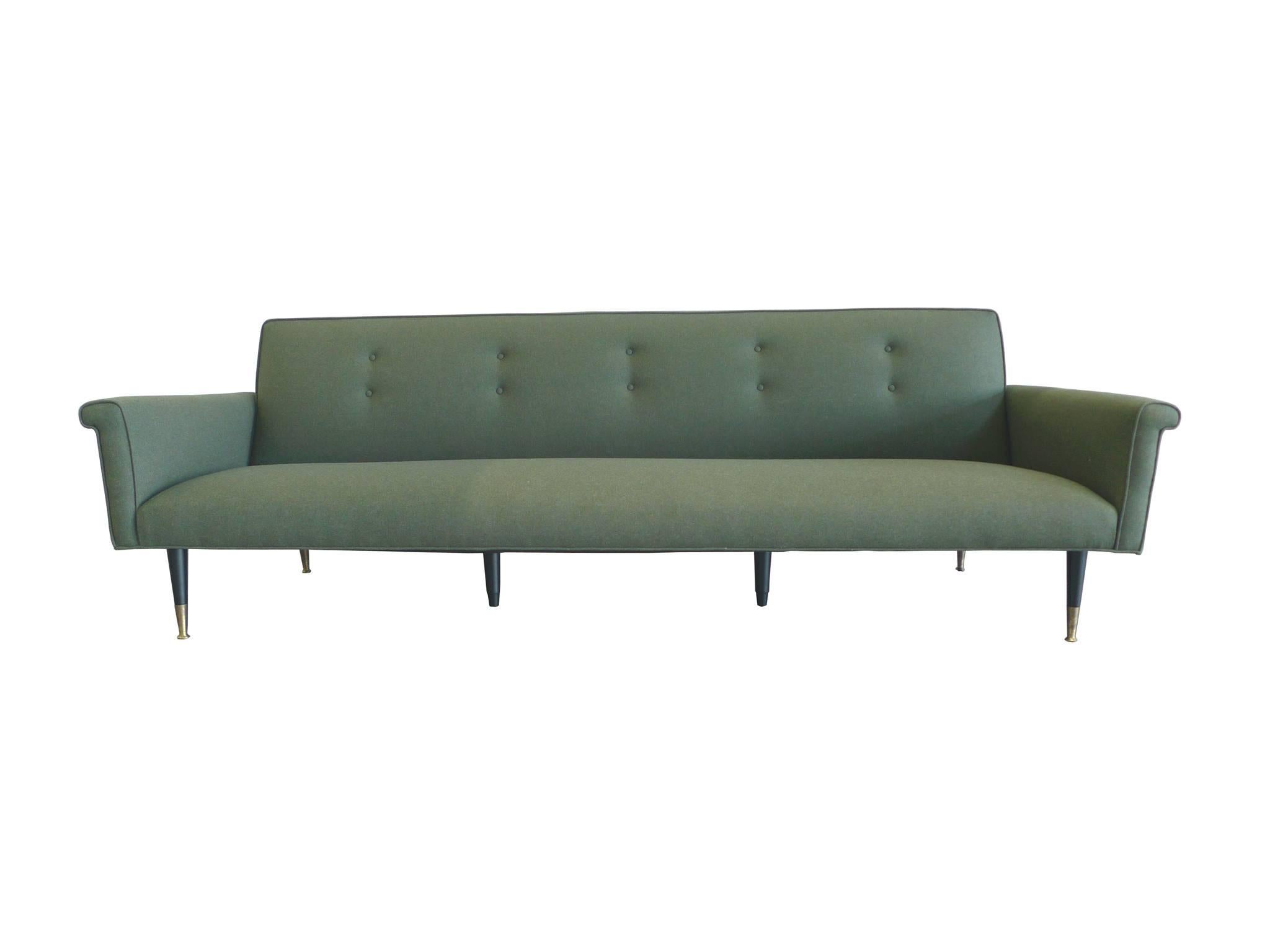 This handsome 1960s sofa is newly reupholstered in a Duralee moss-green wool. Its minimal design takes after the style of Edward Wormley: smooth shapes contoured by elegant piping, a tufted back cushion, and tapering wooden legs with brass accents.