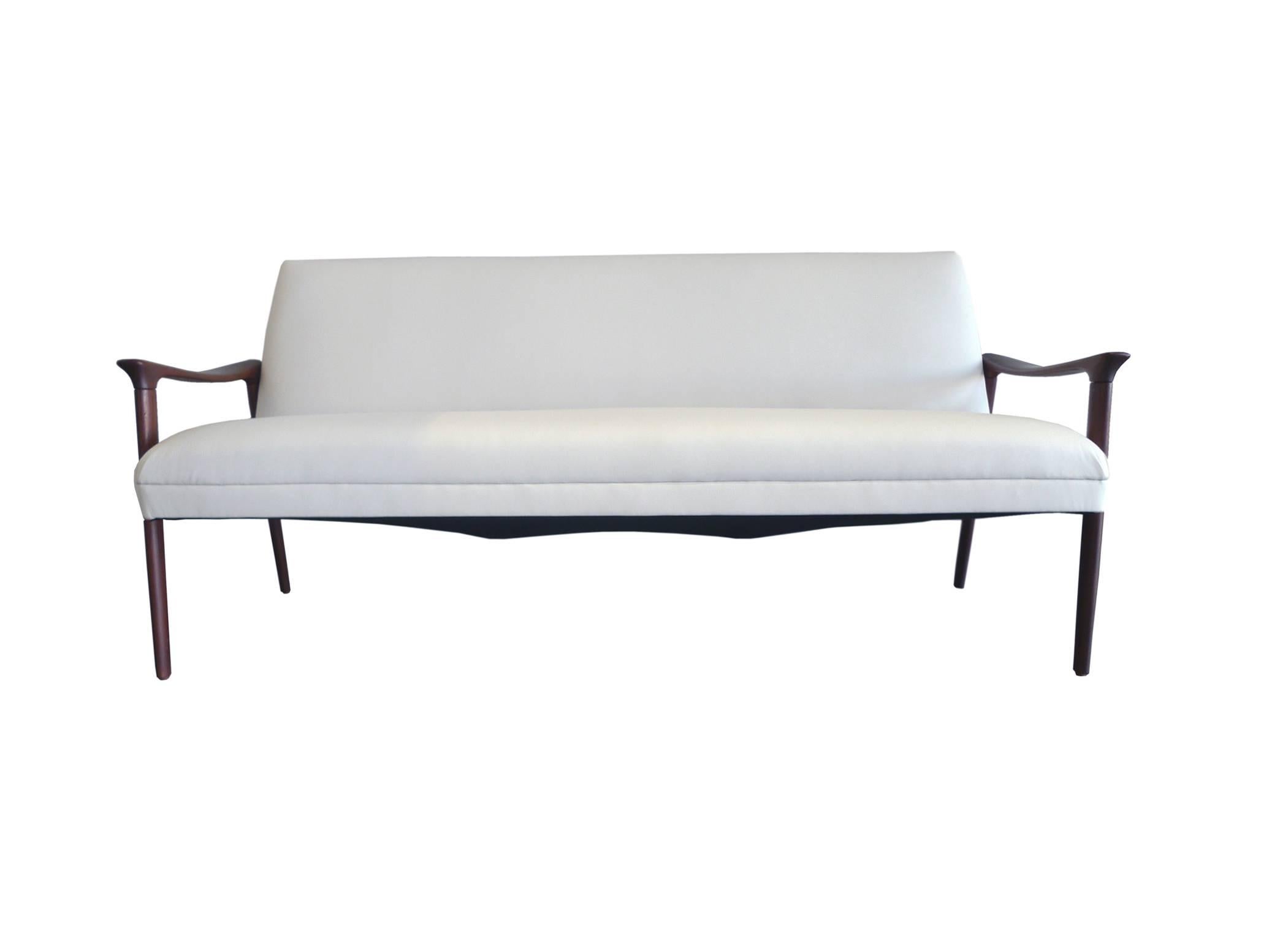This handsome mid-20th century Danish sofa is by Ole Wanscher. It's newly refinished and reupholstered in white vinyl. The frame is a rich red-brown teak; its design is one of clean lines and soft edges. The arms are flat and elegantly slope, while